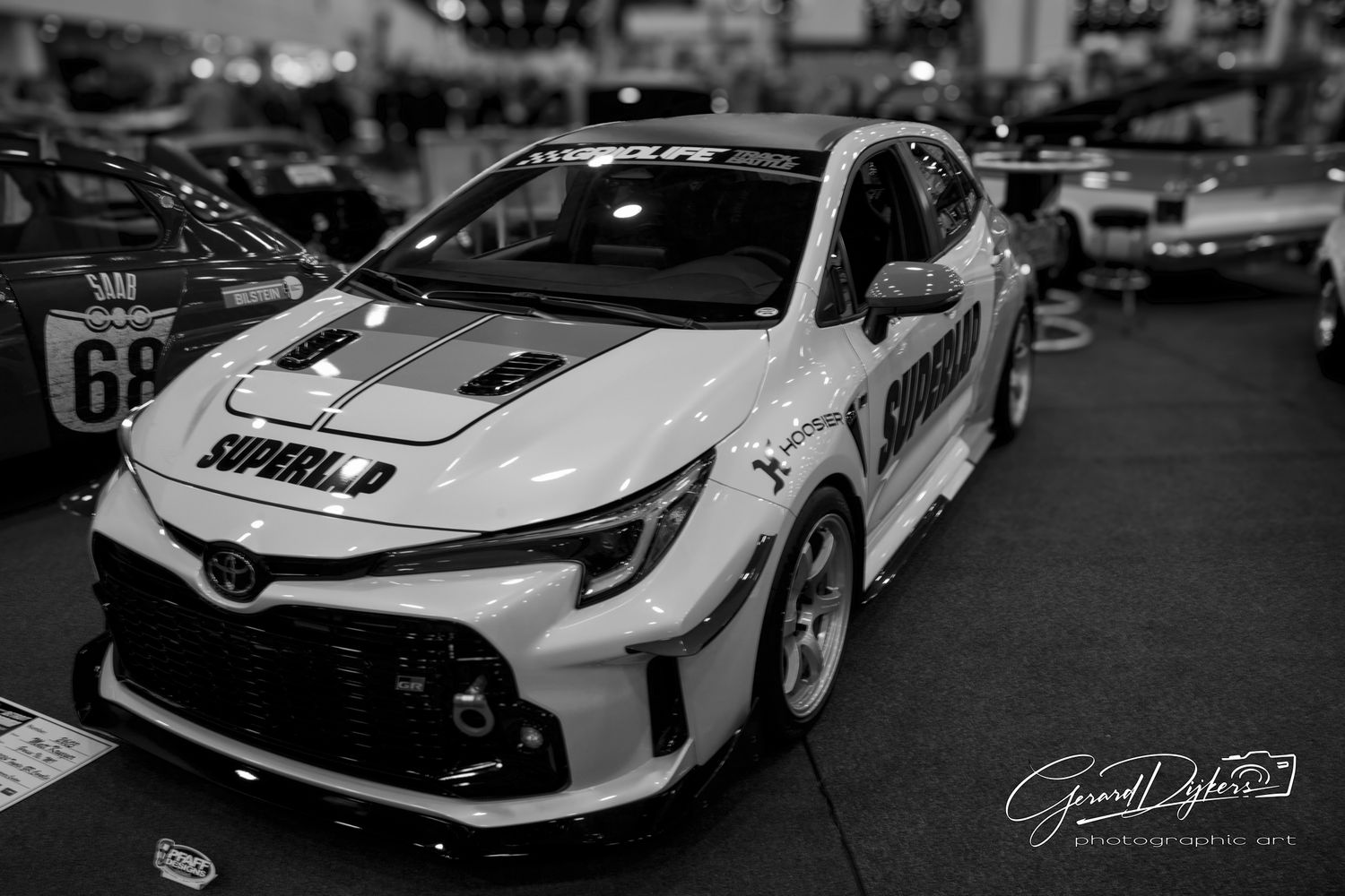 Black and white photo of a modified Toyota Corolla race car with custom body kit and racing livery on display.