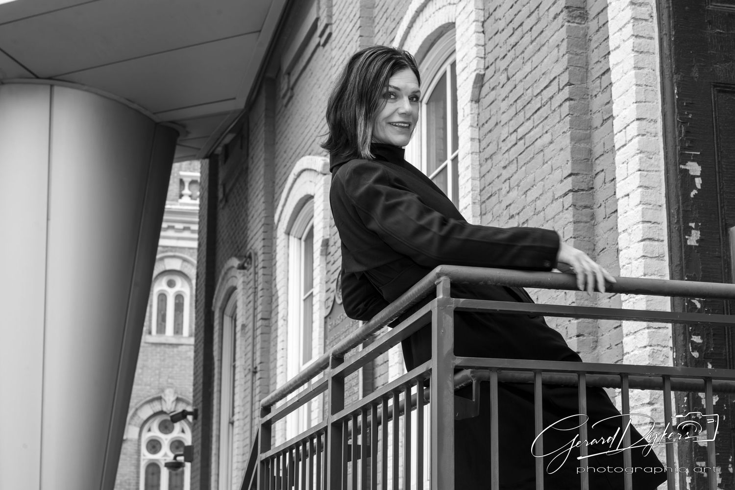 A black and white photograph shows a person ascending stairs in front of a brick building with arched windows.