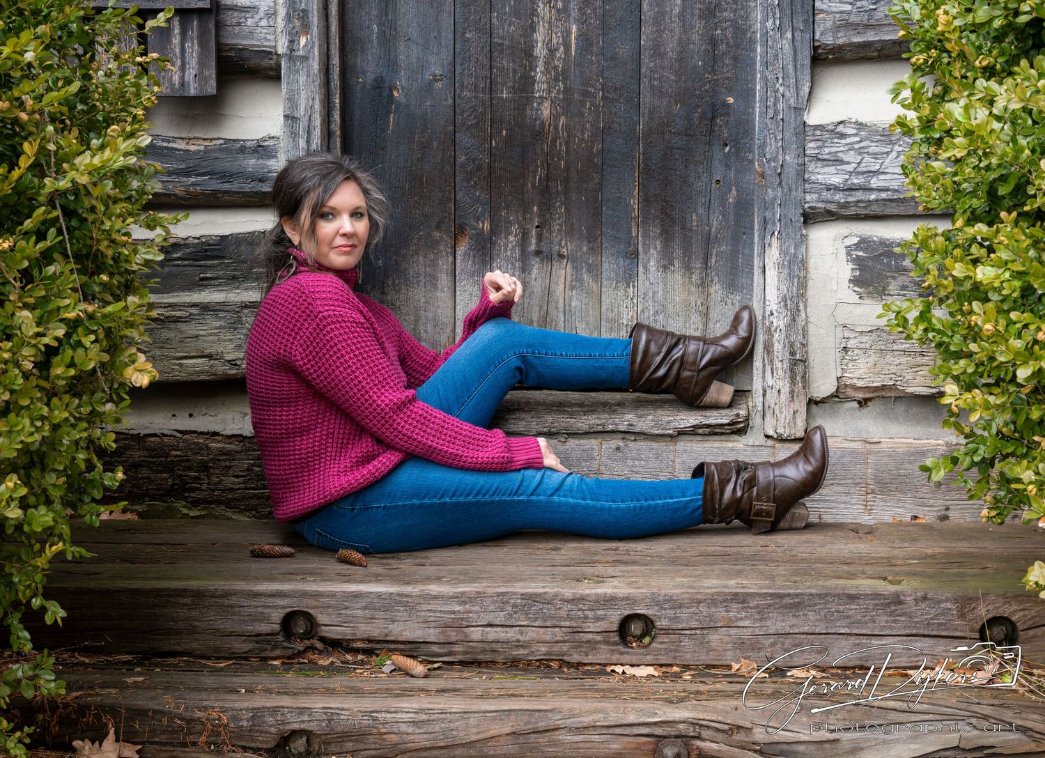 A person in a burgundy sweater and blue jeans relaxes on a rustic wooden porch in a casual pose.