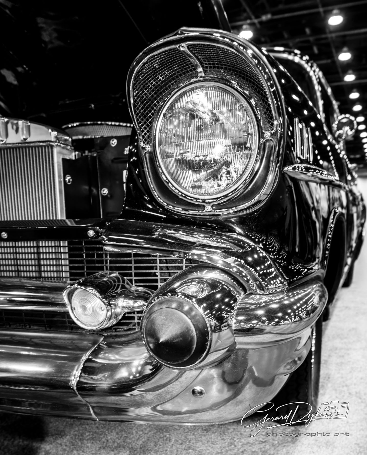 Close-up black and white photo of vintage car headlights and chrome trim details at an auto show.