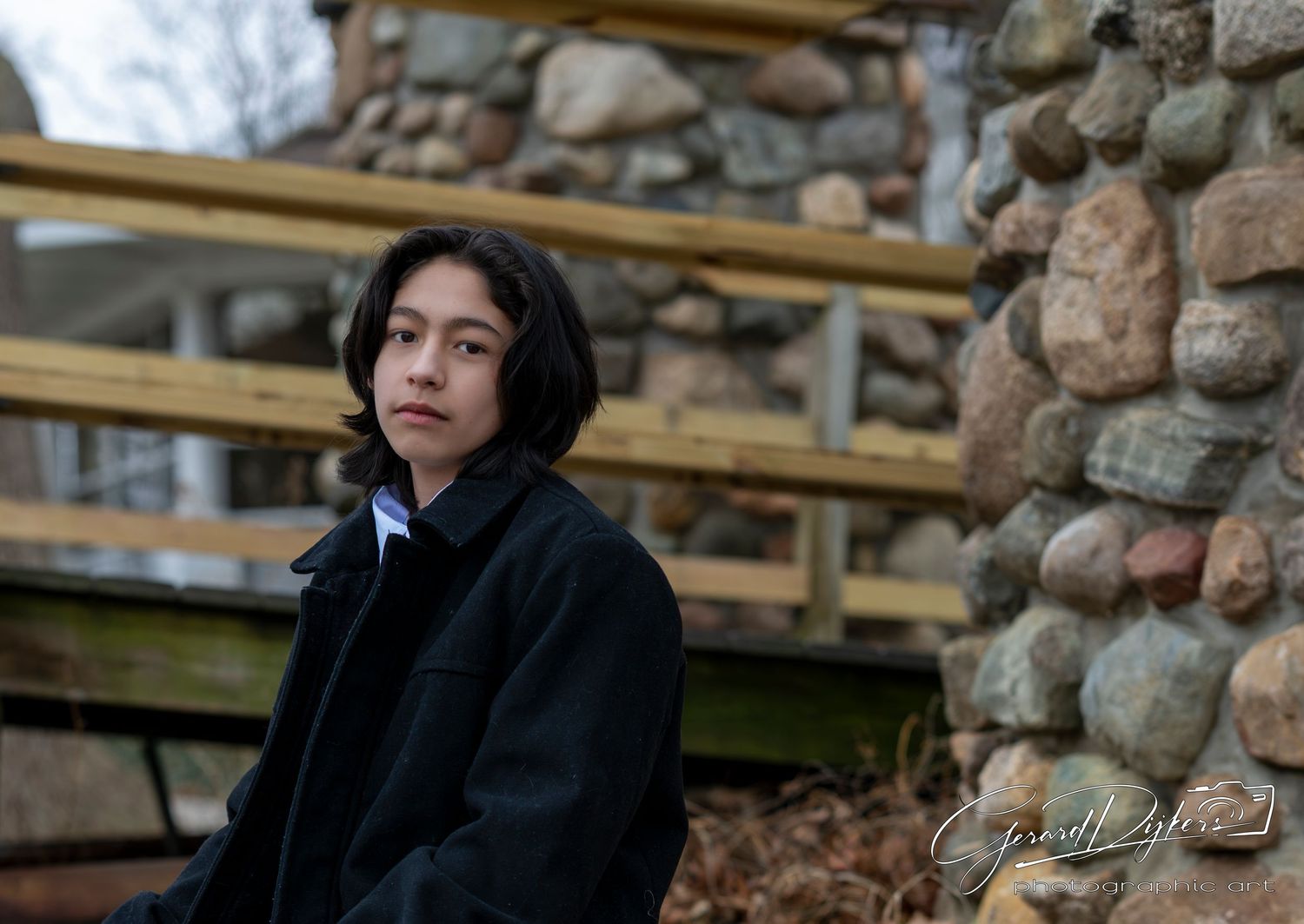Person in dark clothing sits thoughtfully against stone wall background in moody outdoor setting.