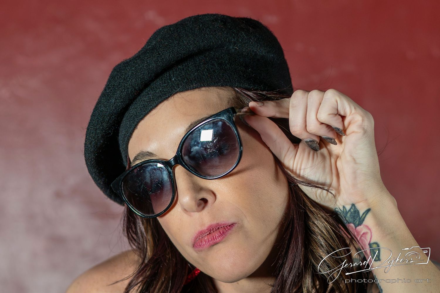 Person in black hat and sunglasses striking different poses against a red background.