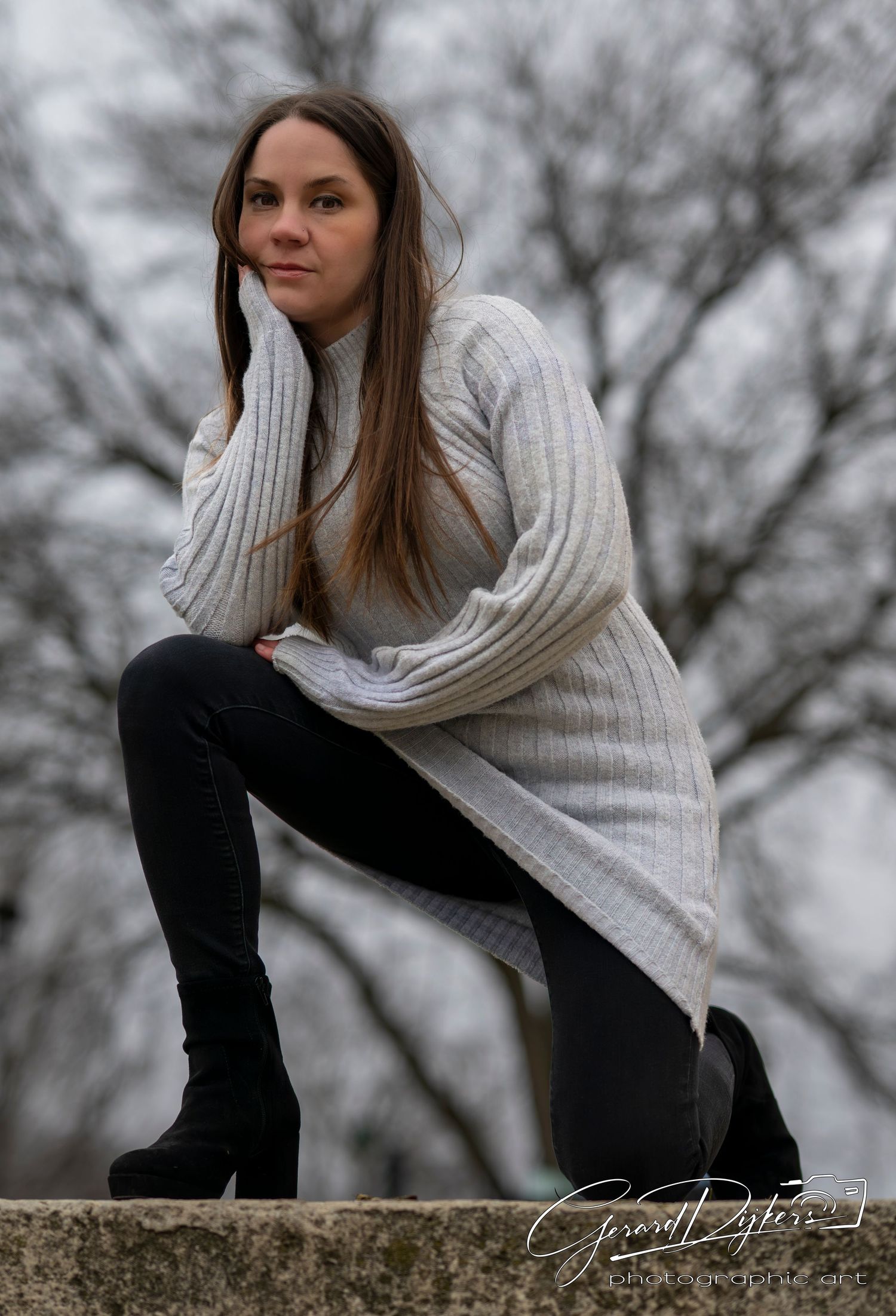 A figure in a cozy white sweater sits thoughtfully on a stone wall against a moody winter backdrop.