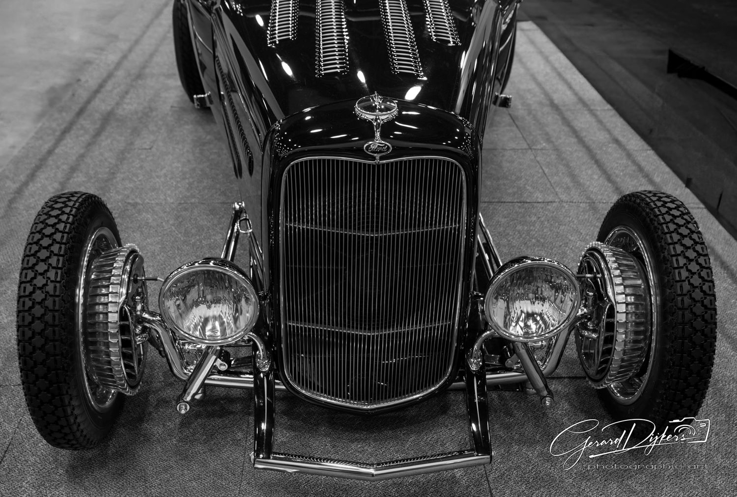 Black and white photo of a vintage hot rod car with custom chrome wheels and exposed engine components.