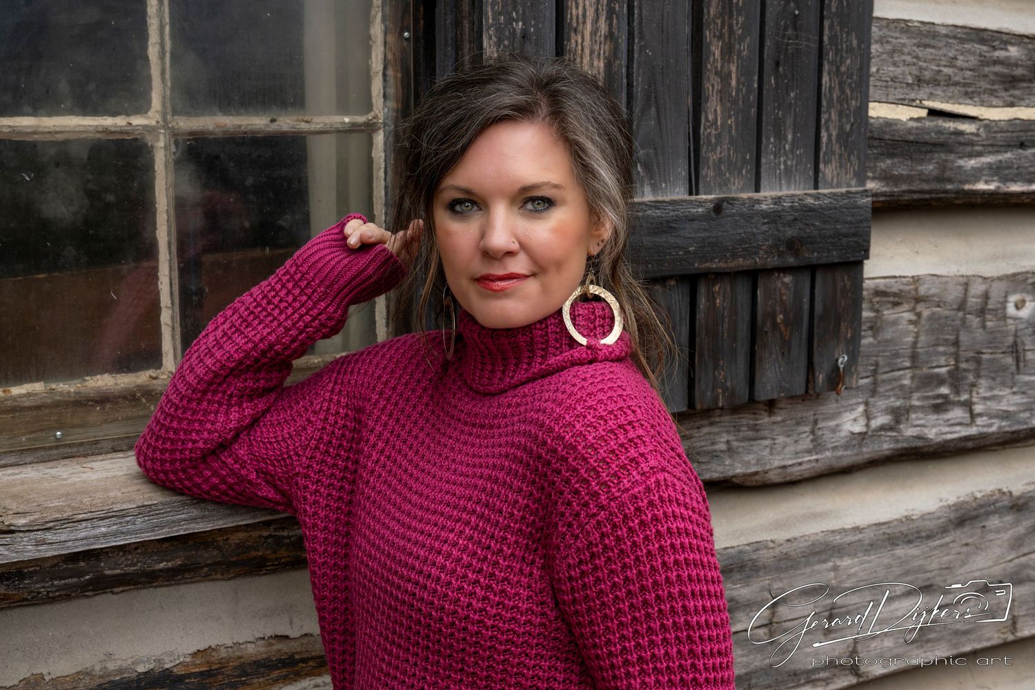 Woman in burgundy knit sweater poses against rustic wooden wall in outdoor photoshoot.