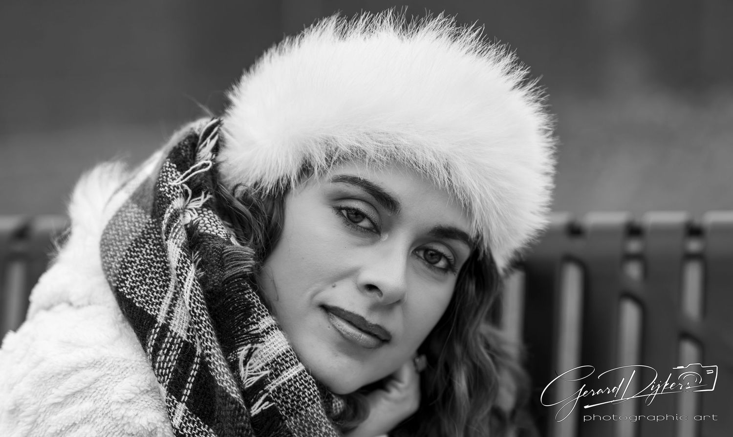 Close-up black and white portrait of woman wearing white fur hat in winter setting.