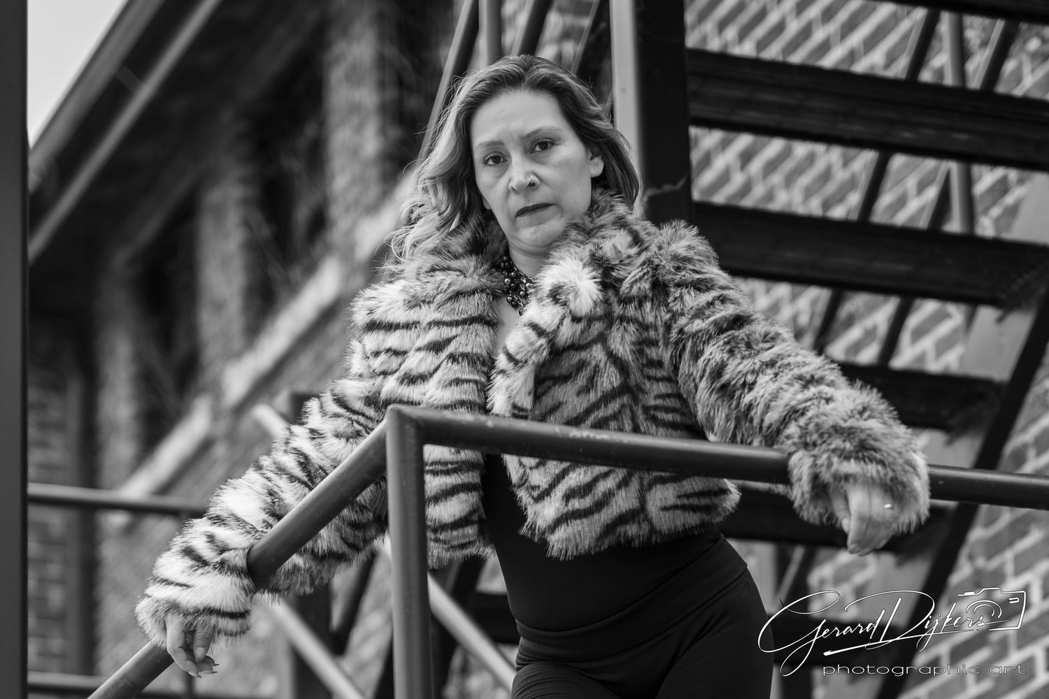 Person wearing a tiger print fur coat poses against an urban backdrop with fire escapes and brick buildings.