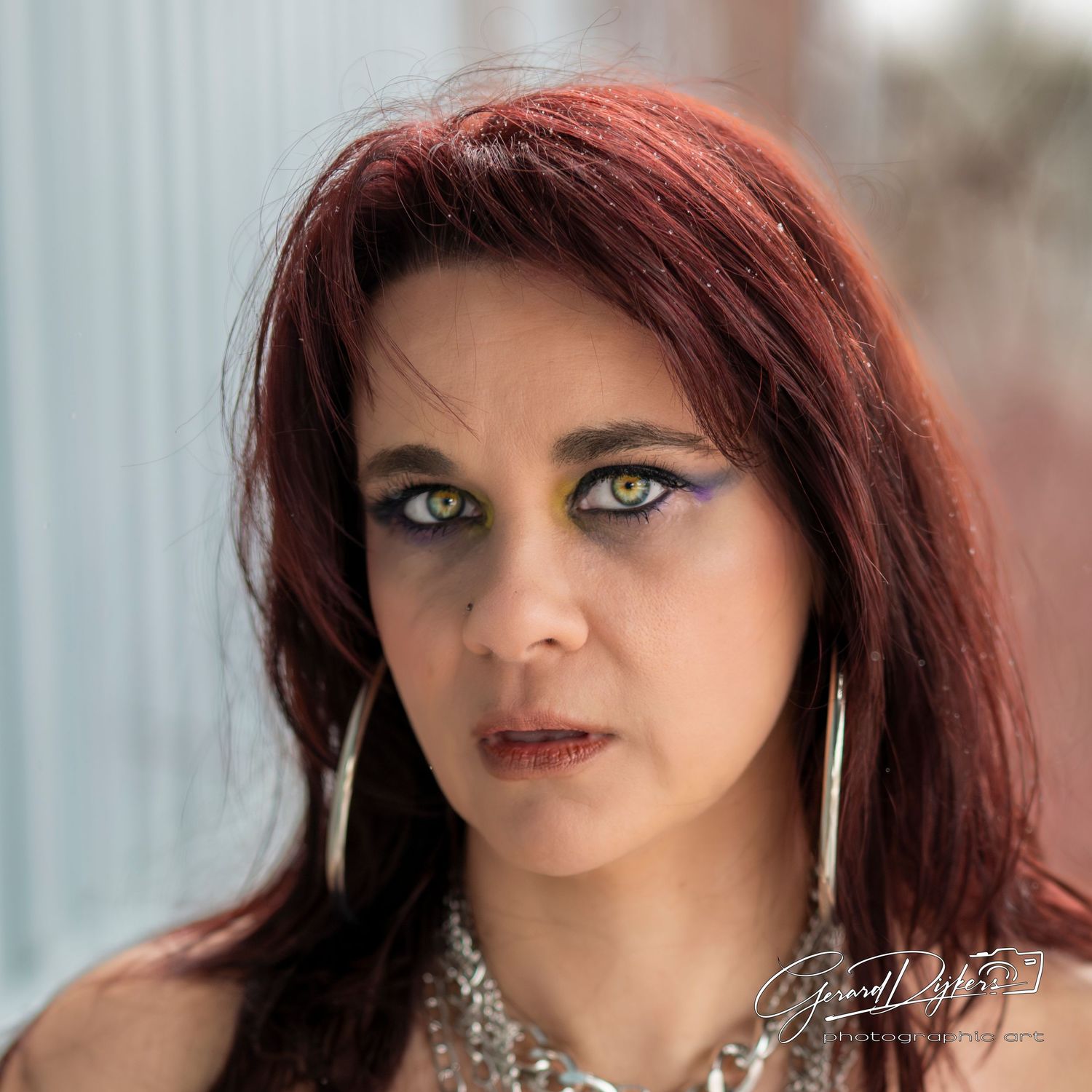 A person with burgundy hair and glamorous makeup poses in a series of close-up portrait shots wearing sparkly jewelry.