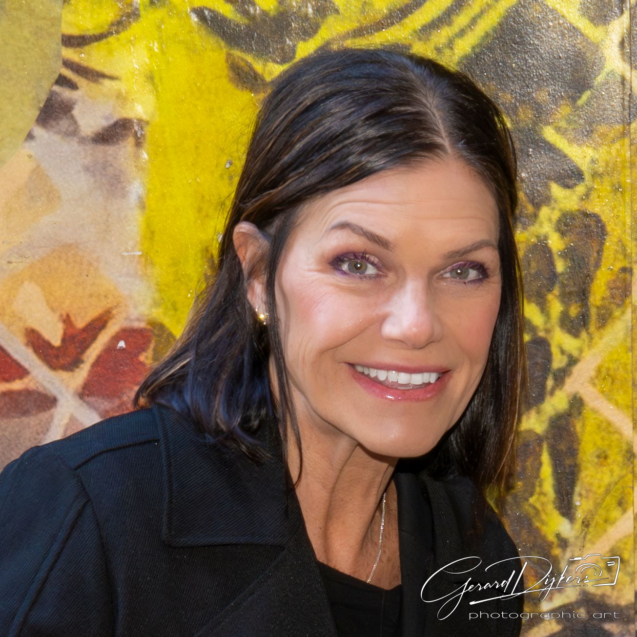 Portrait against vibrant yellow graffiti wall with dark hair and bright smile.