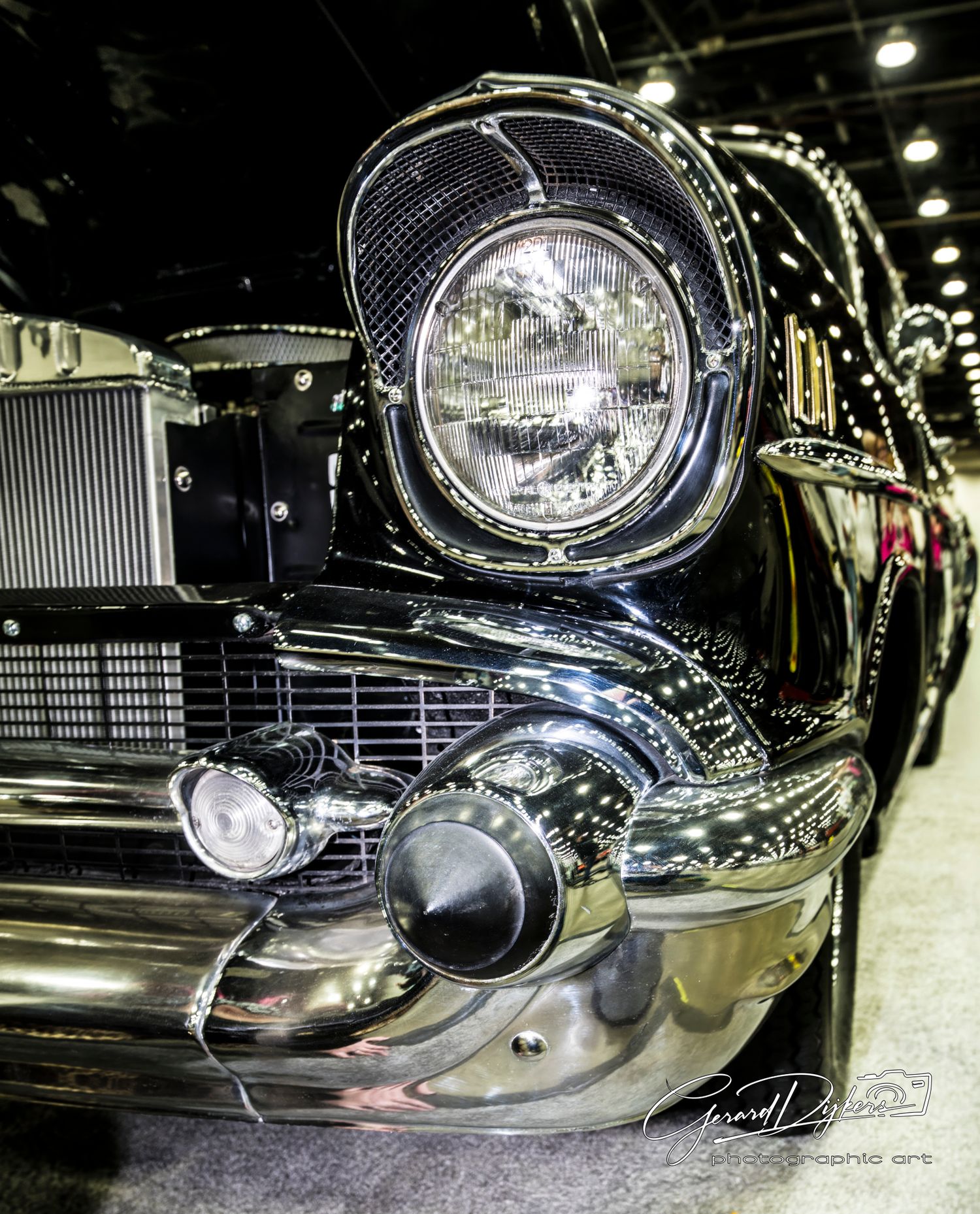 Close-up detail of a classic car's chrome headlight and front grille showing glossy black paint and polished metal trim.