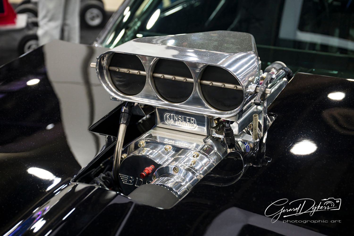 Detailed black and white photograph of vintage car engine parts with chrome accents and reflective surfaces.