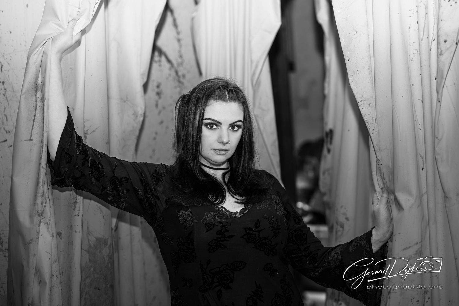 A dark and moody black and white portrait of someone with dramatic lighting and white curtains in the background.