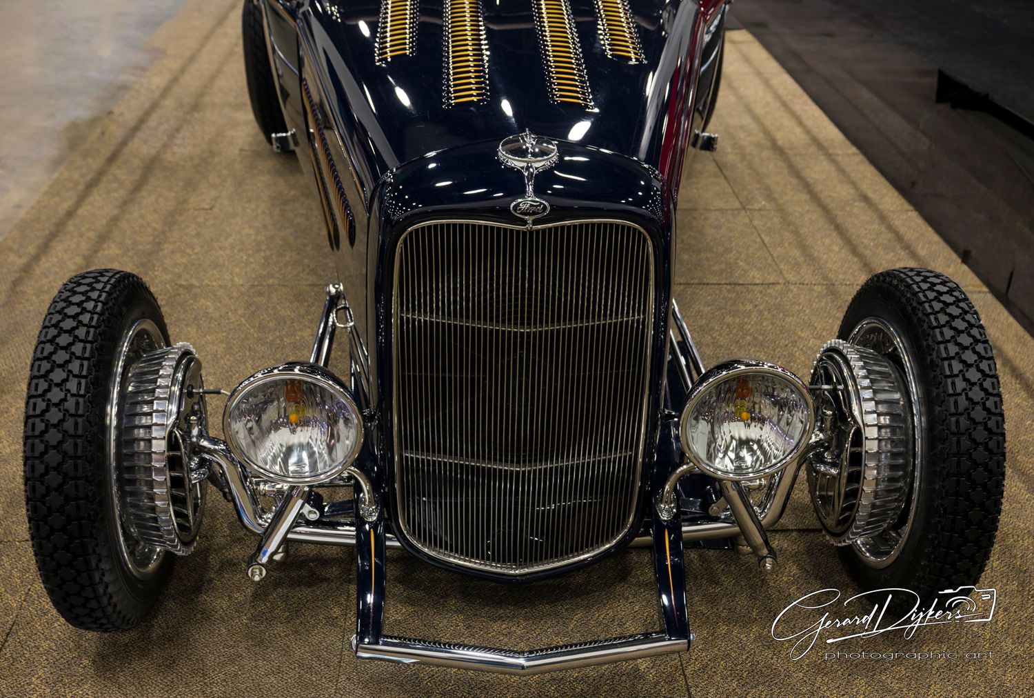 Vintage hot rod cars lined up in a row showing detailed front grille and wheel views in sepia tones.
