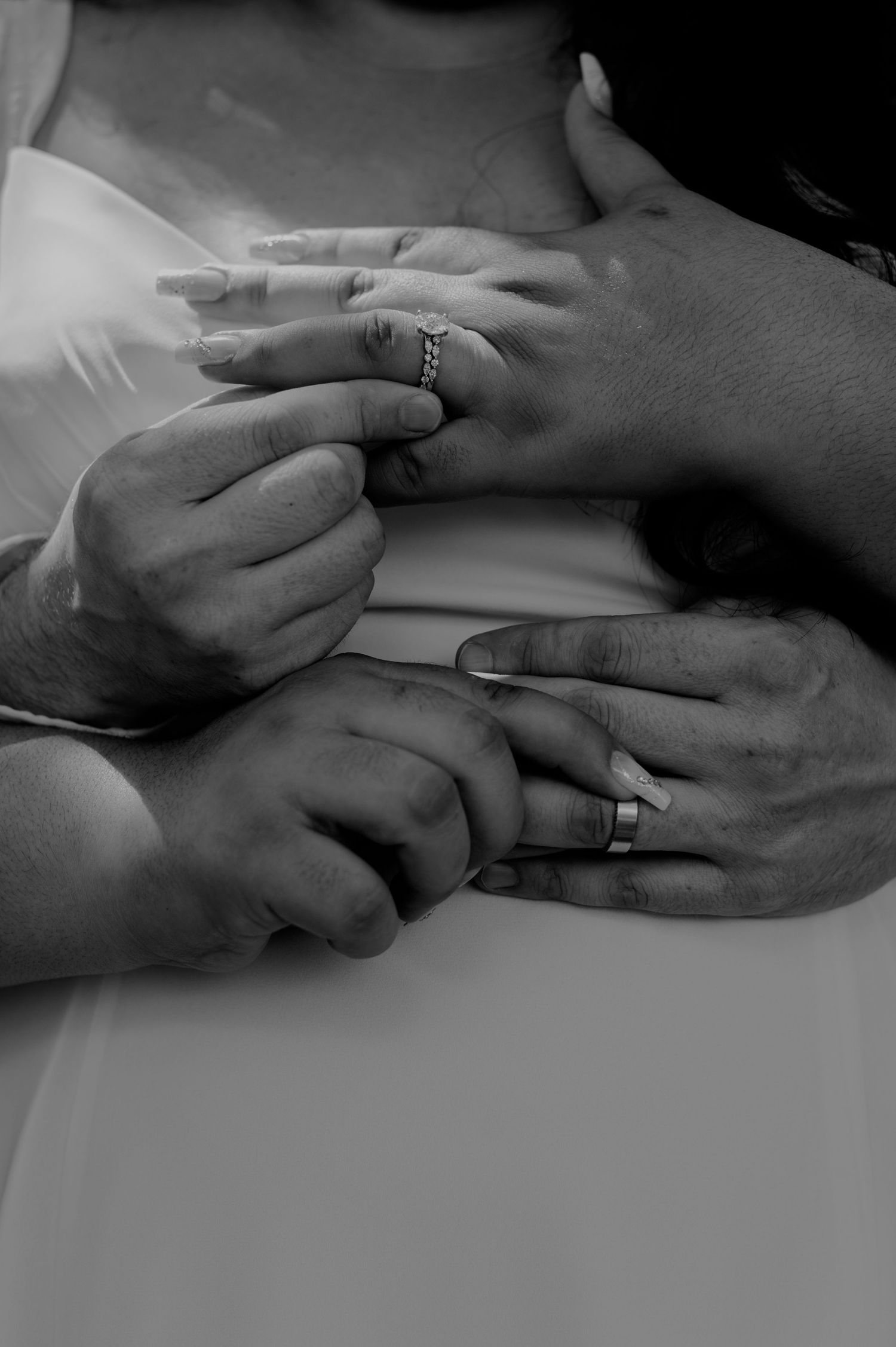 Black and white close-up of hands with wedding rings showing a tender moment during a ceremony.