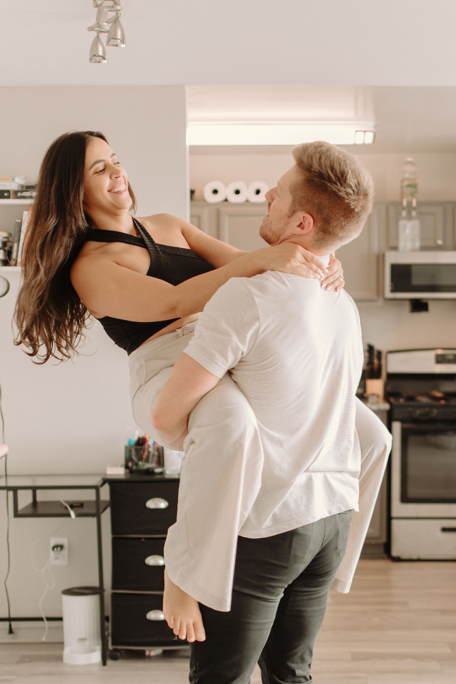 Couple dancing and laughing together in their modern kitchen with soft lighting.