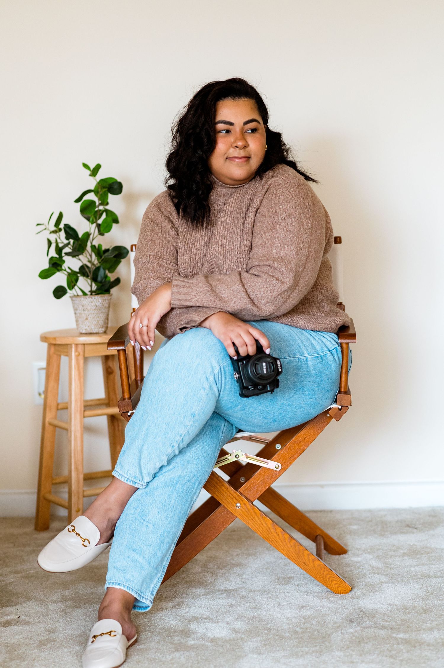 Portrait of a person in a brown sweater and jeans sitting on a wooden director's chair.