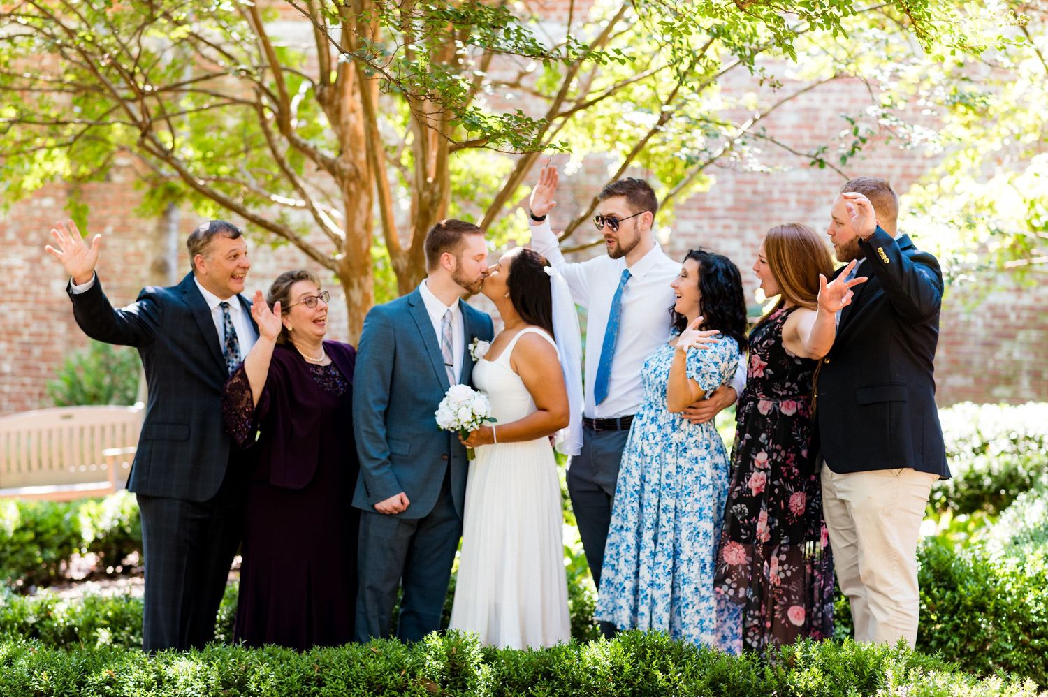 Wedding party celebrating in garden with stone architecture and blooming flowers.