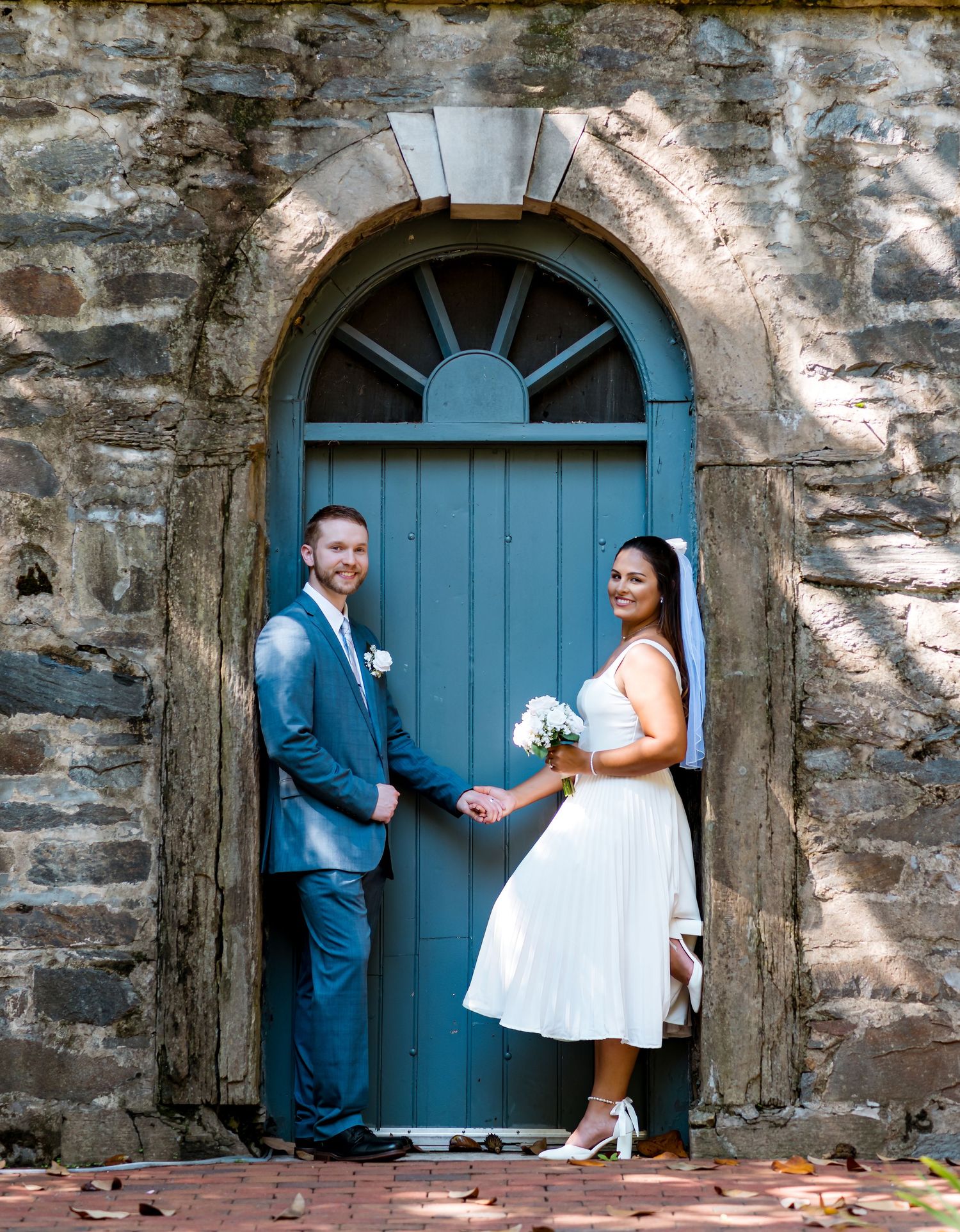 Couple poses in blue arched doorway of historic stone building on wedding day.