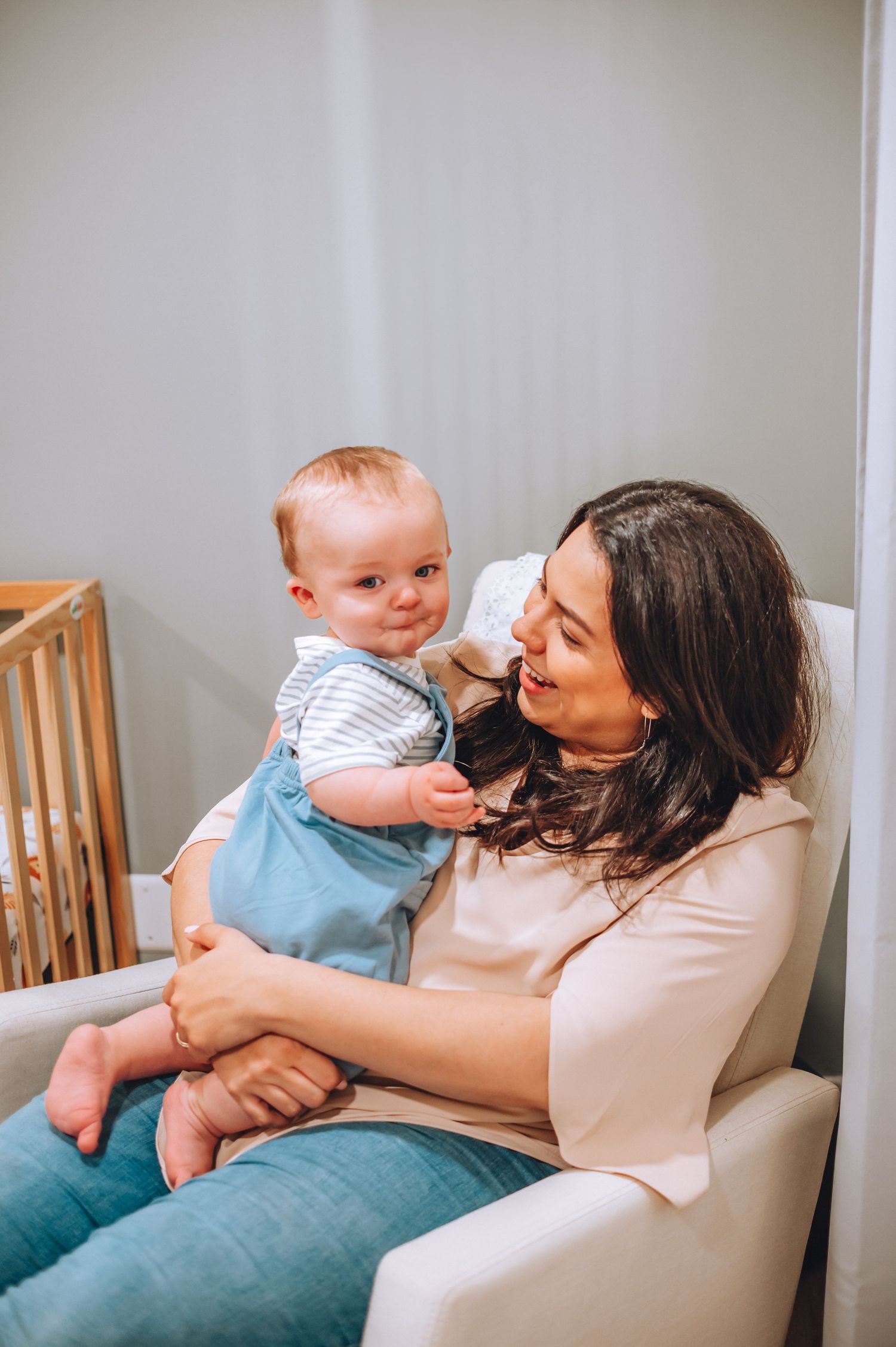 Sweet bonding moment between parent and baby sitting in a cozy armchair beside a wooden crib.