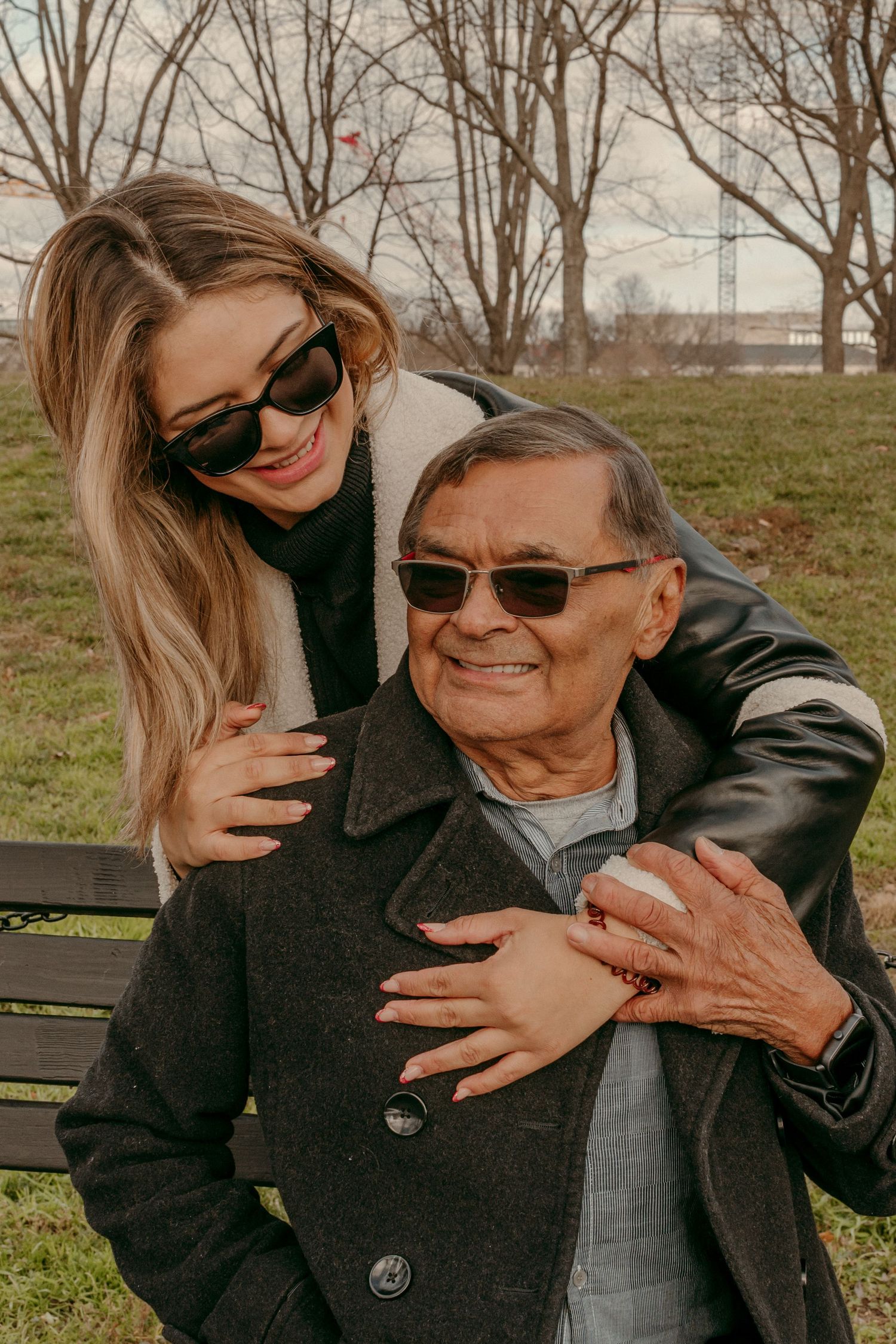 Two people in dark coats sharing a warm embrace while sitting on a park bench.