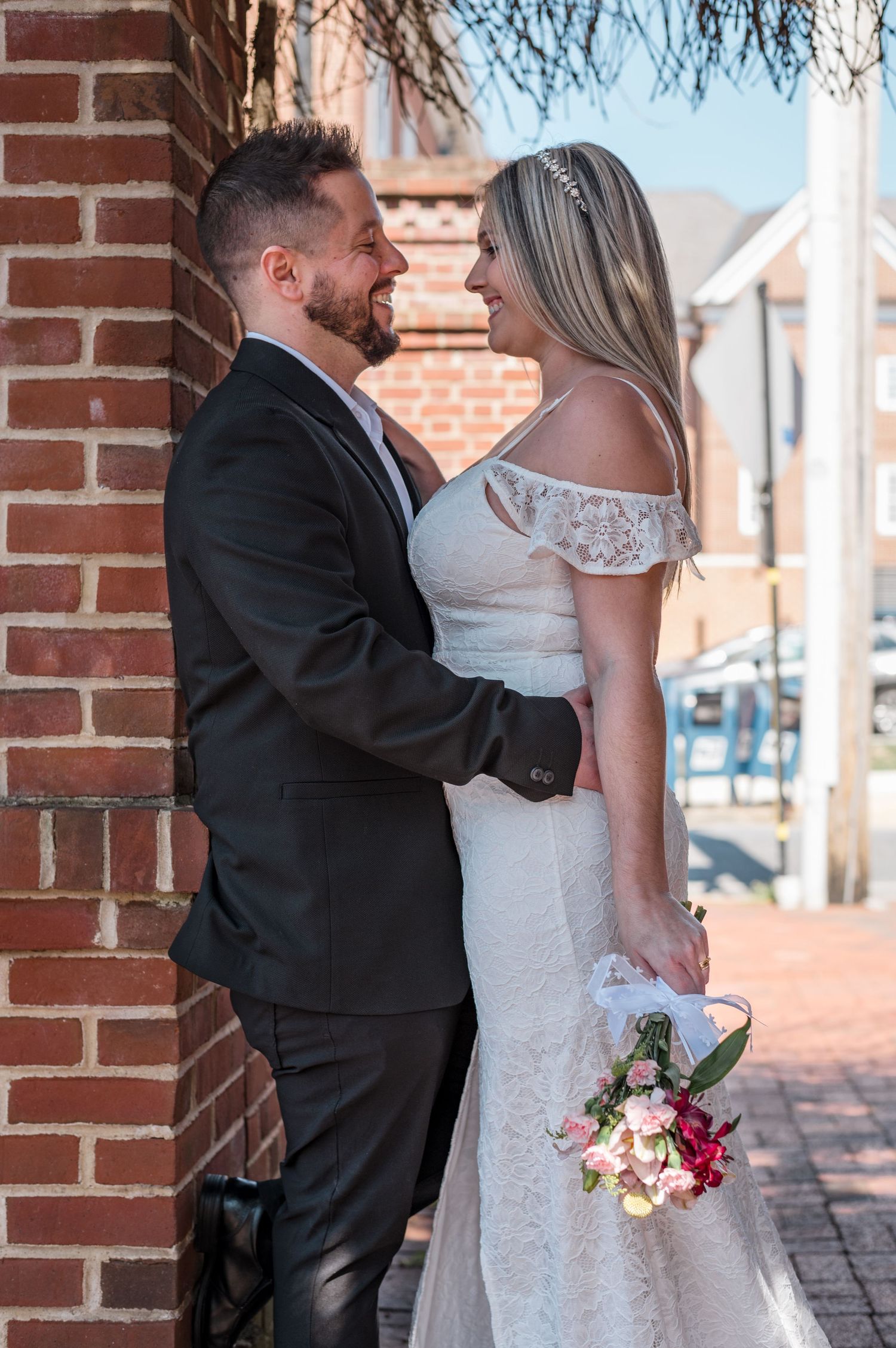 A couple embraces against a brick wall during their wedding photoshoot.