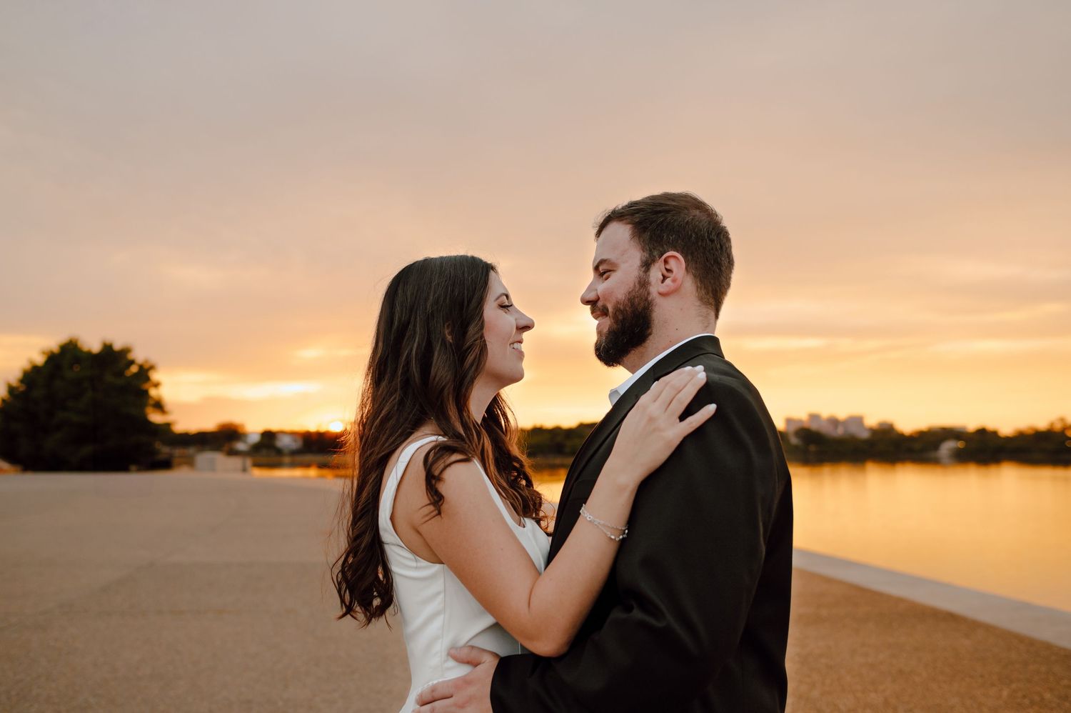 Silhouetted couple embracing in a romantic pose against a golden sunset sky over water.