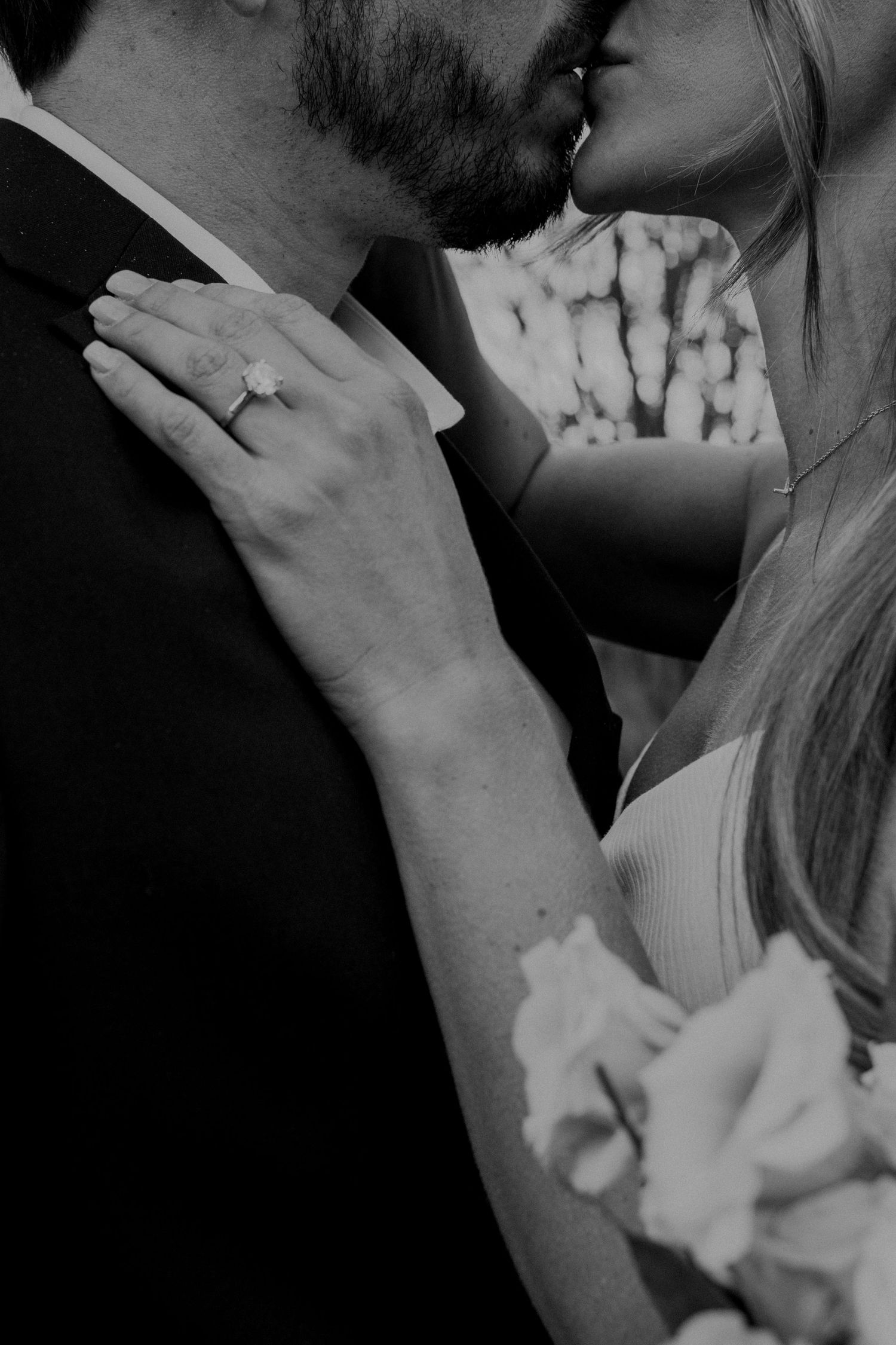 Black and white intimate moment between couple showing an engagement ring and romantic embrace.