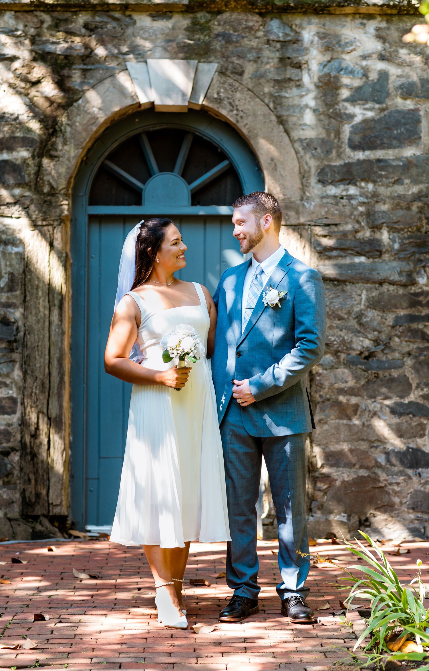 Newlyweds posing in front of blue arched door on stone building with garden elements.