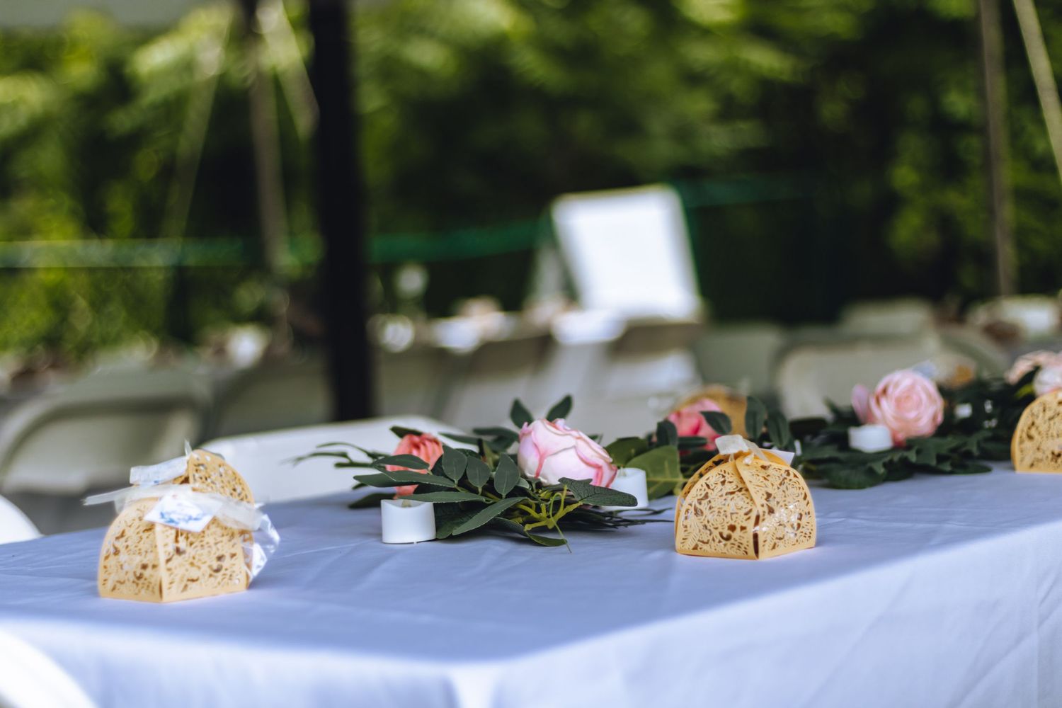 Elegant table setting with pink roses and decorative elements on a light blue tablecloth at an outdoor event.