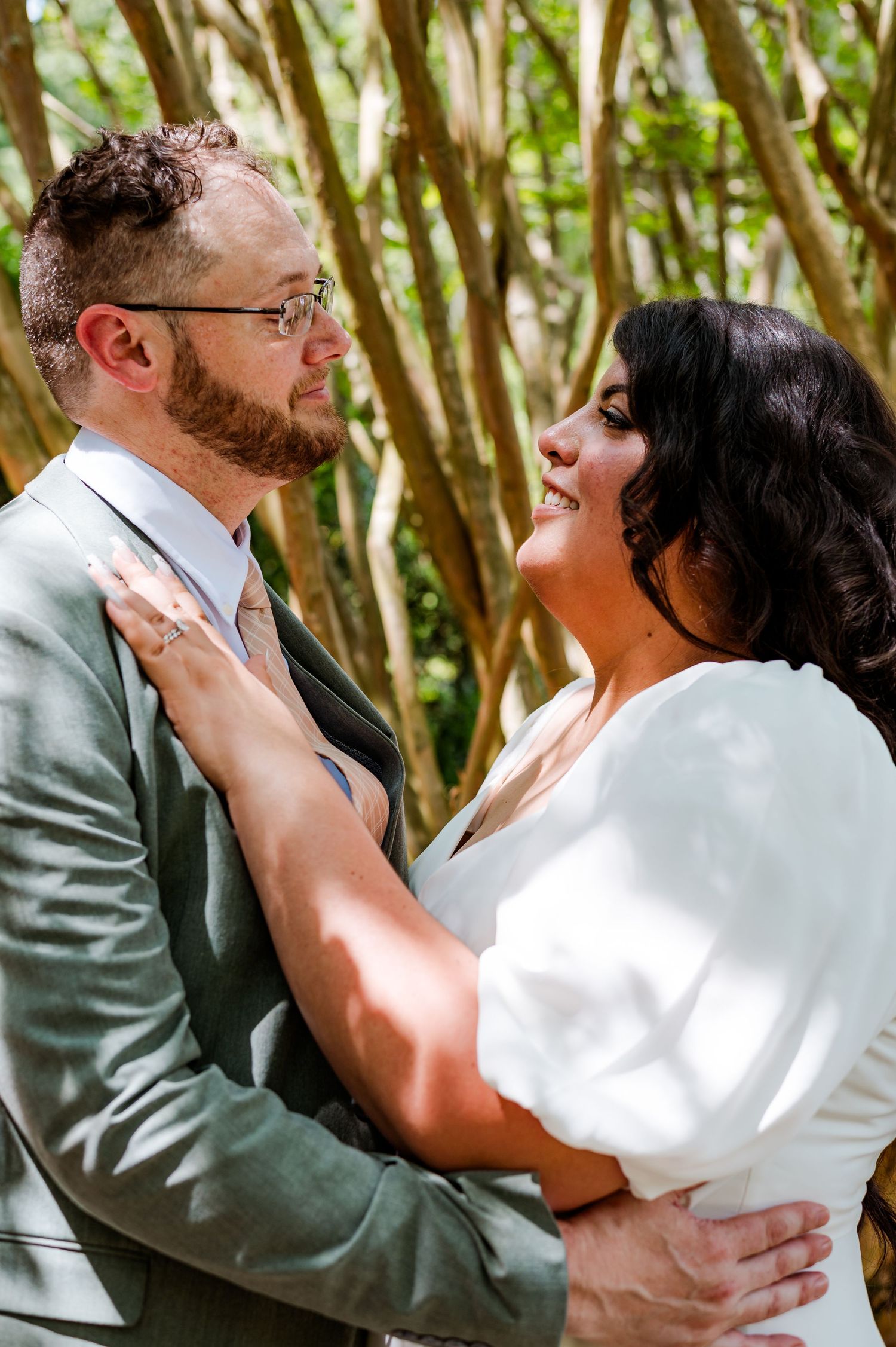 A romantic wedding moment captured between a couple embracing outdoors with lush greenery in the background.