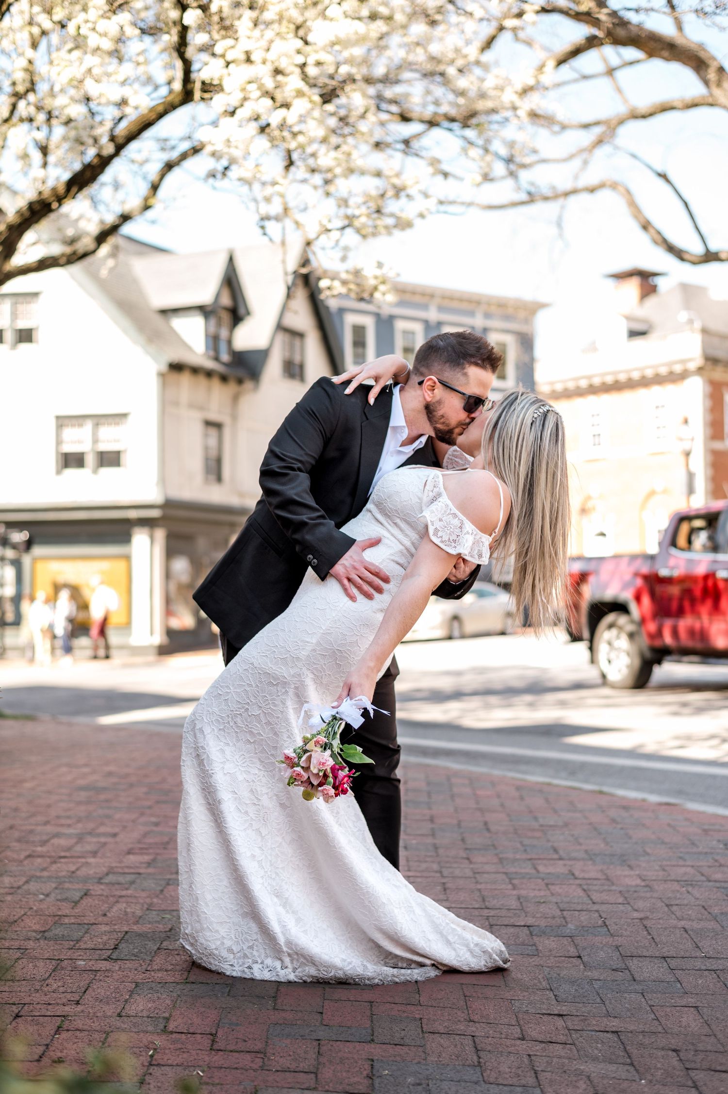 A romantic wedding photo on brick sidewalk with blooming cherry blossoms in spring.