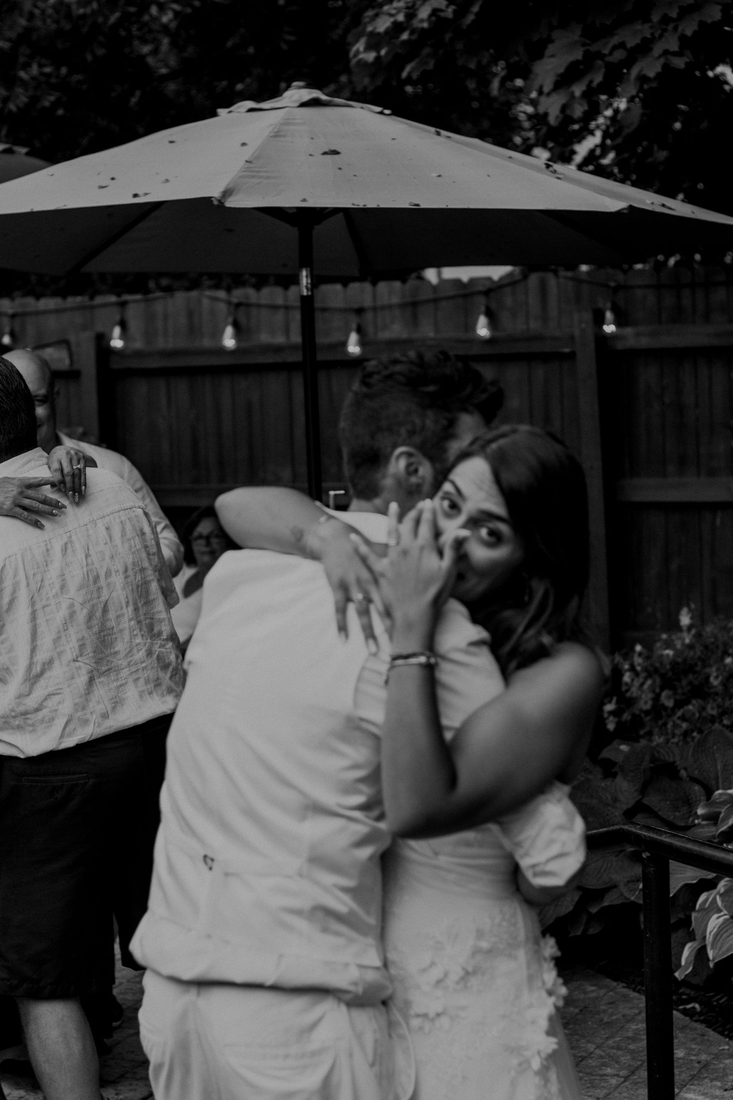 A couple shares a tender moment under a patio umbrella in black and white photography.