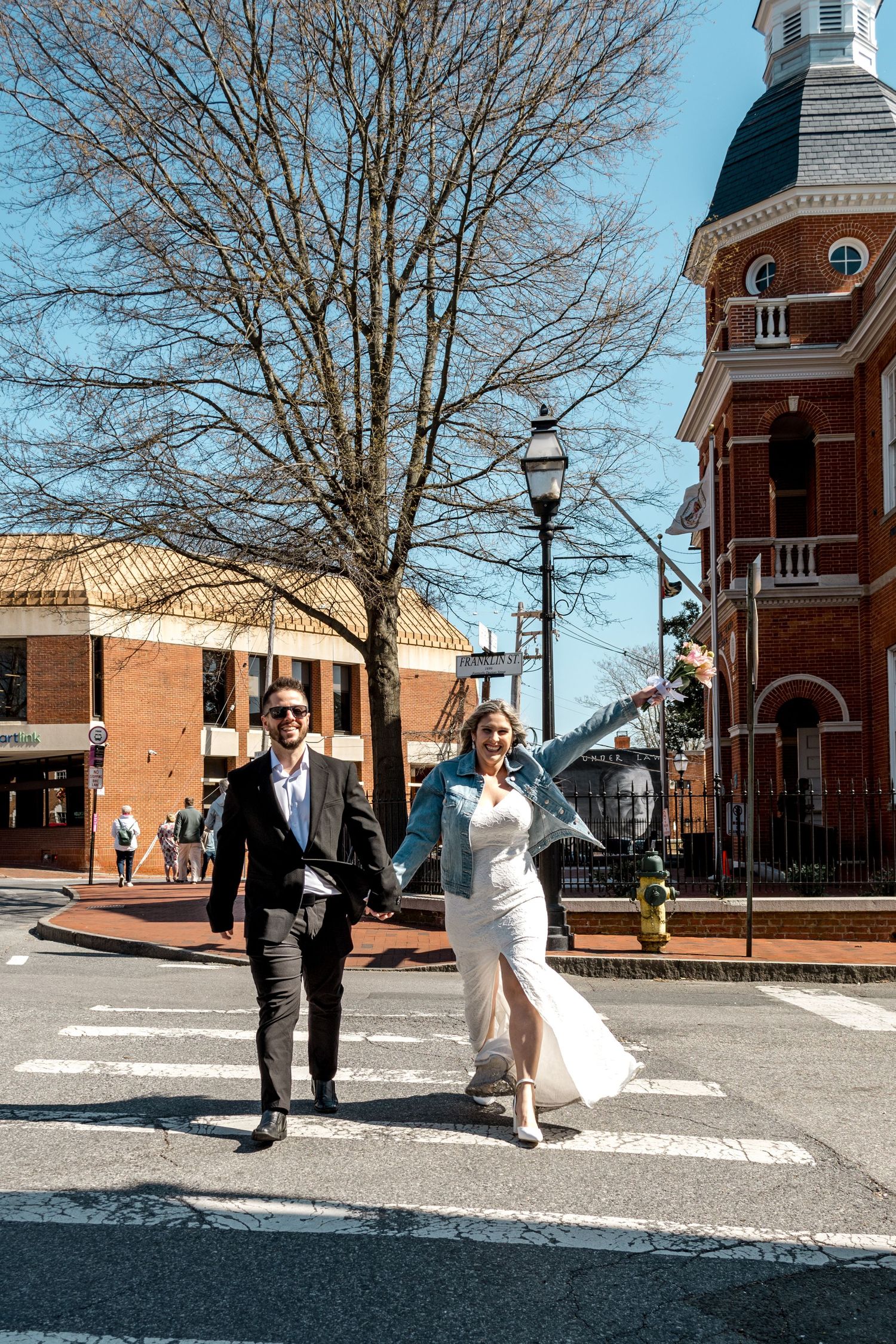 Wedding couple walking through downtown with historic architecture and bare winter trees.