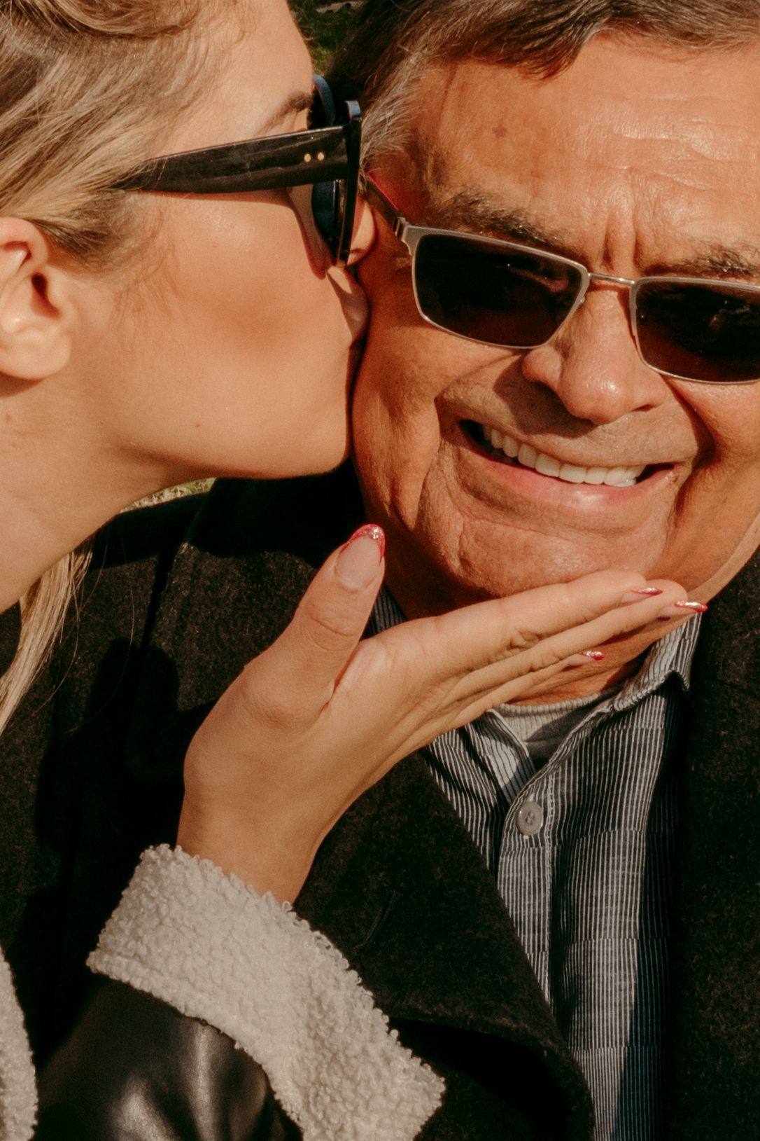 Close up of two people wearing sunglasses sharing tender moment outdoors.