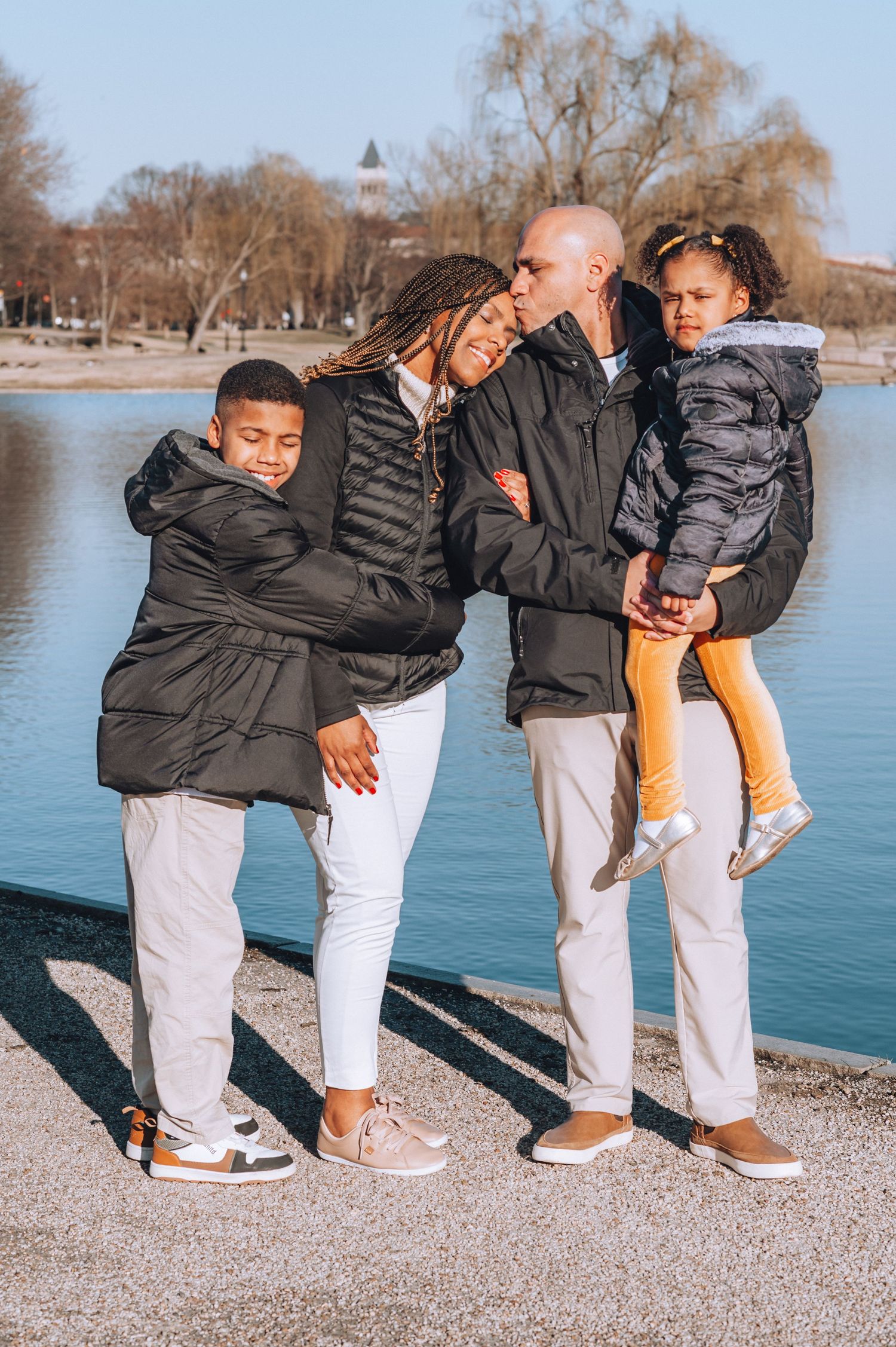 Family of four in matching winter coats posing by a lake on a crisp day.
