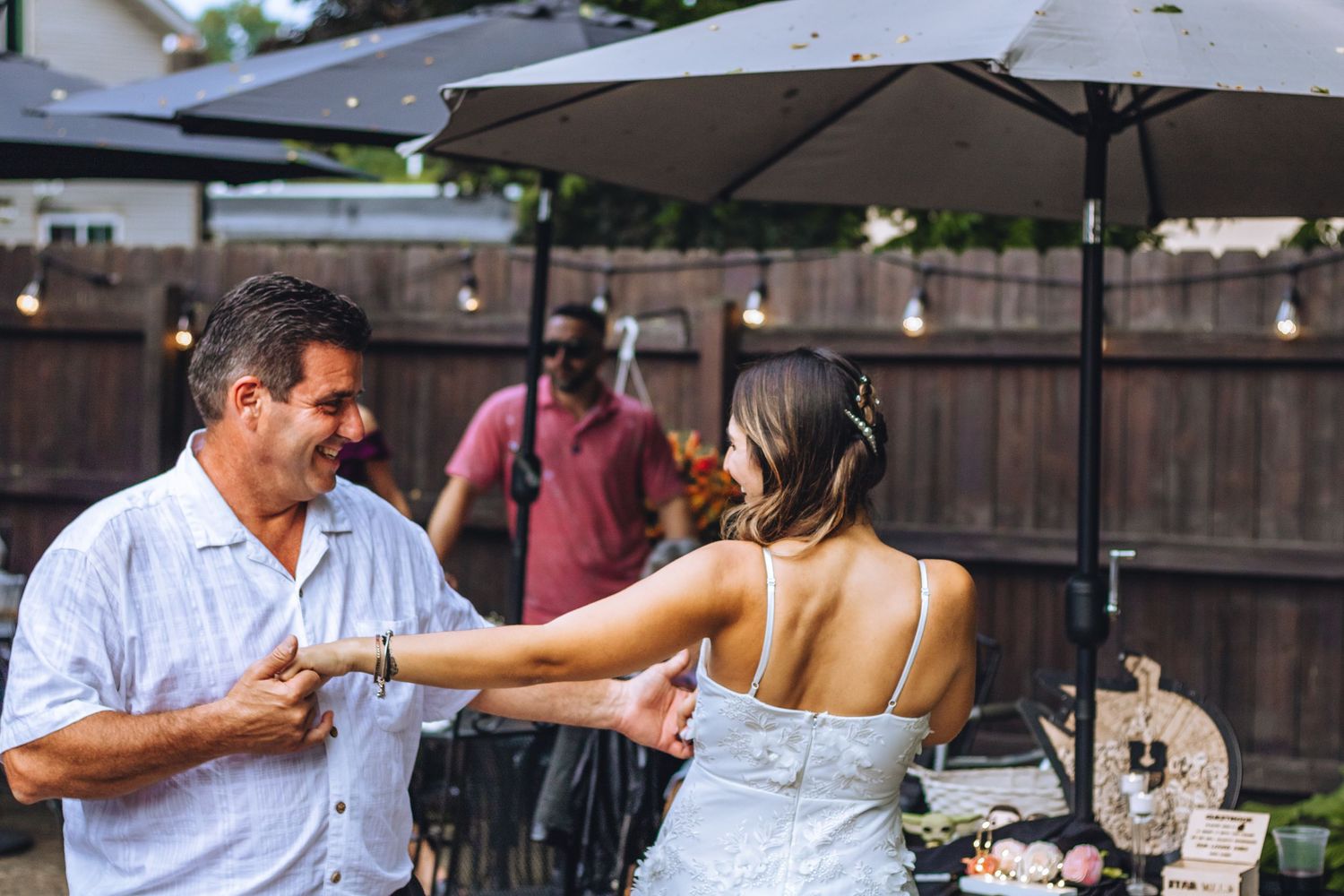 A couple dances together at an outdoor wedding reception under market umbrellas and string lights.