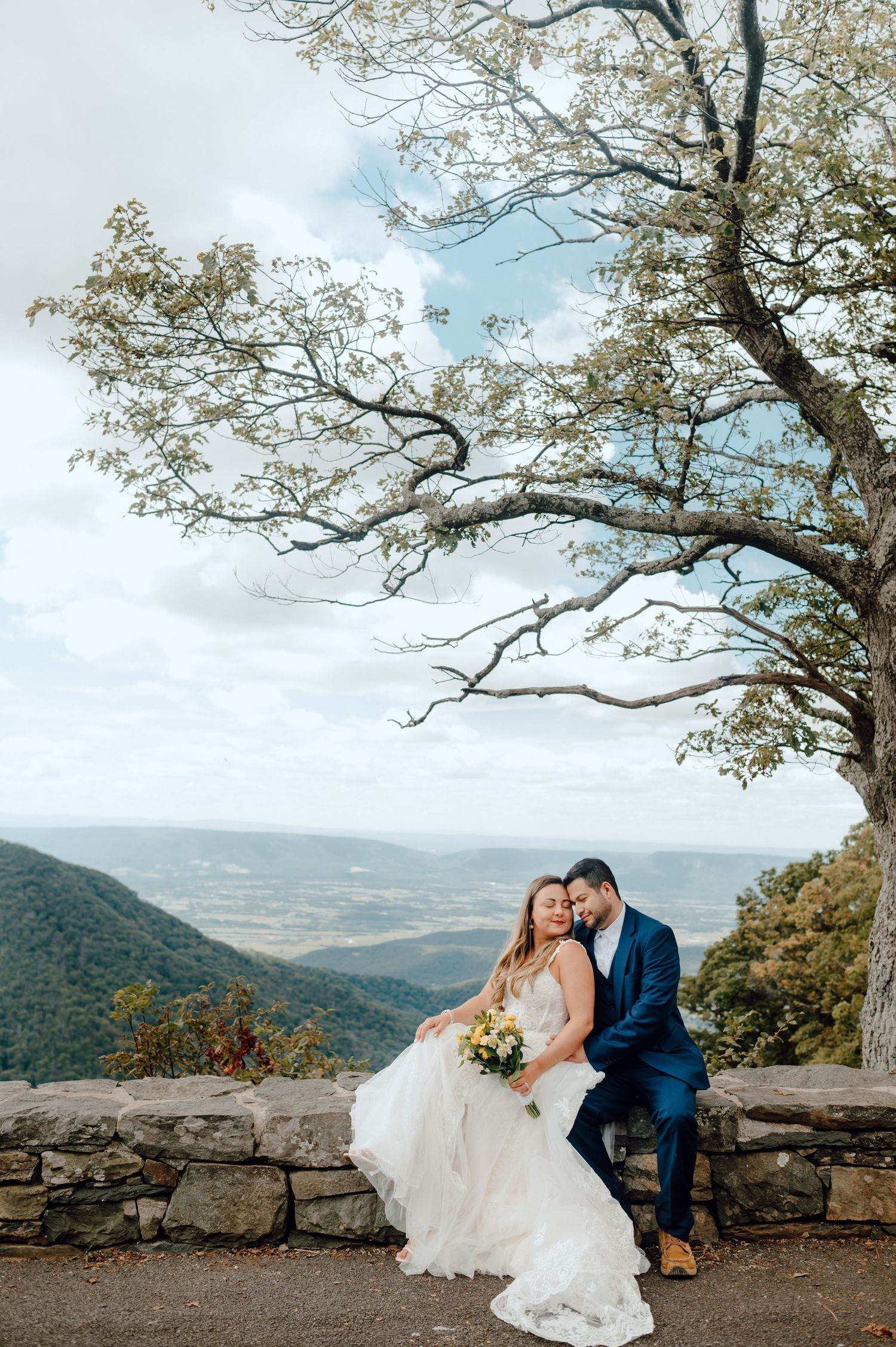 Romantic moment captured at a scenic mountain overlook with stone wall on a cloudy day.
