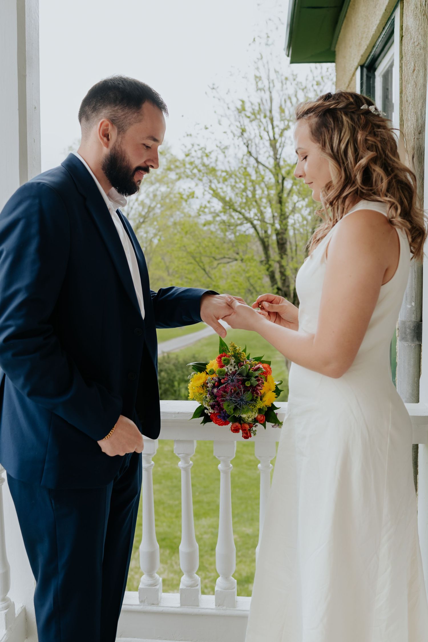A wedding couple shares a candid moment together on a white porch balcony during their first look.