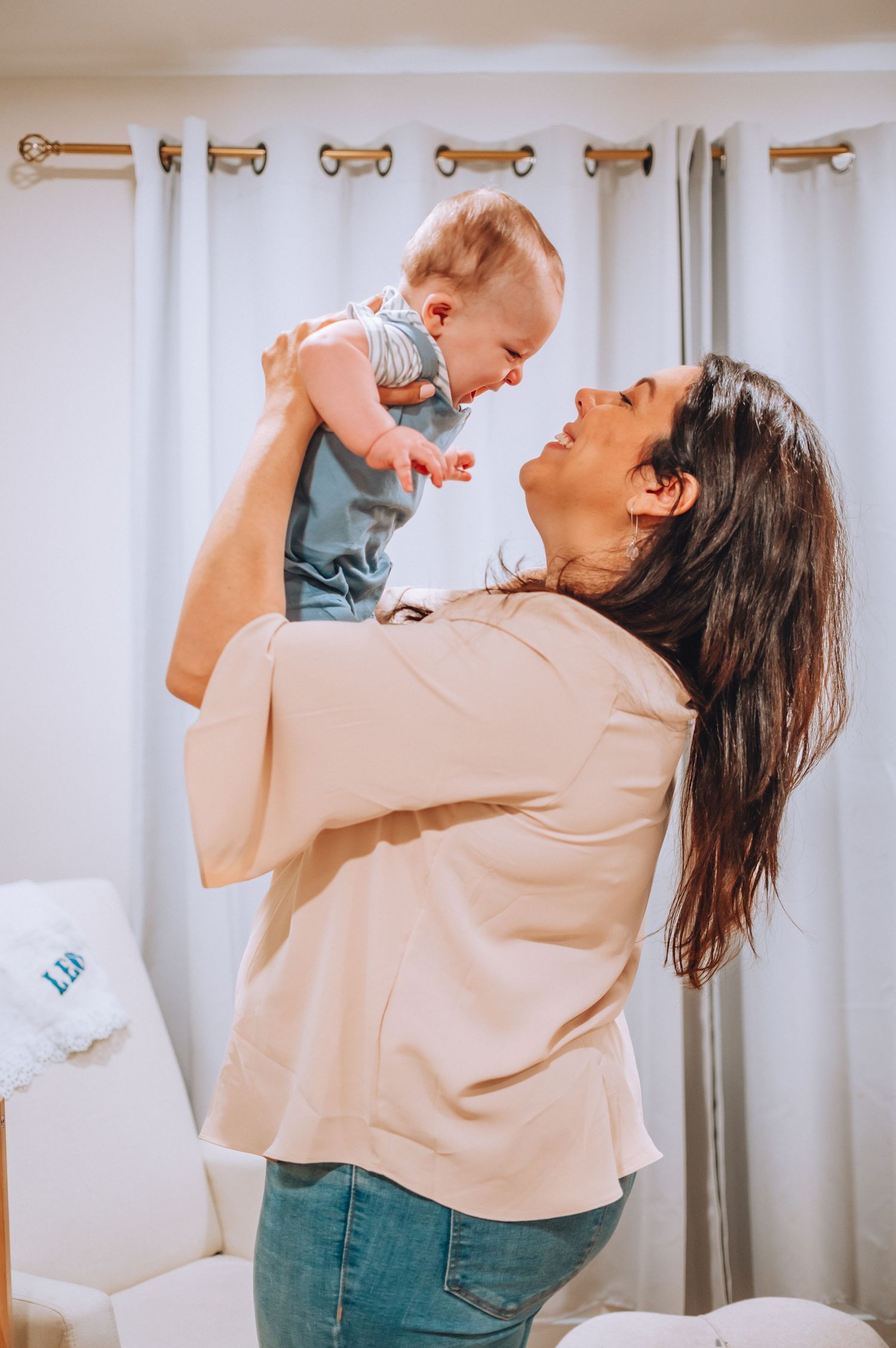 Parent lifting baby in the air during a playful moment in a nursery with white curtains.