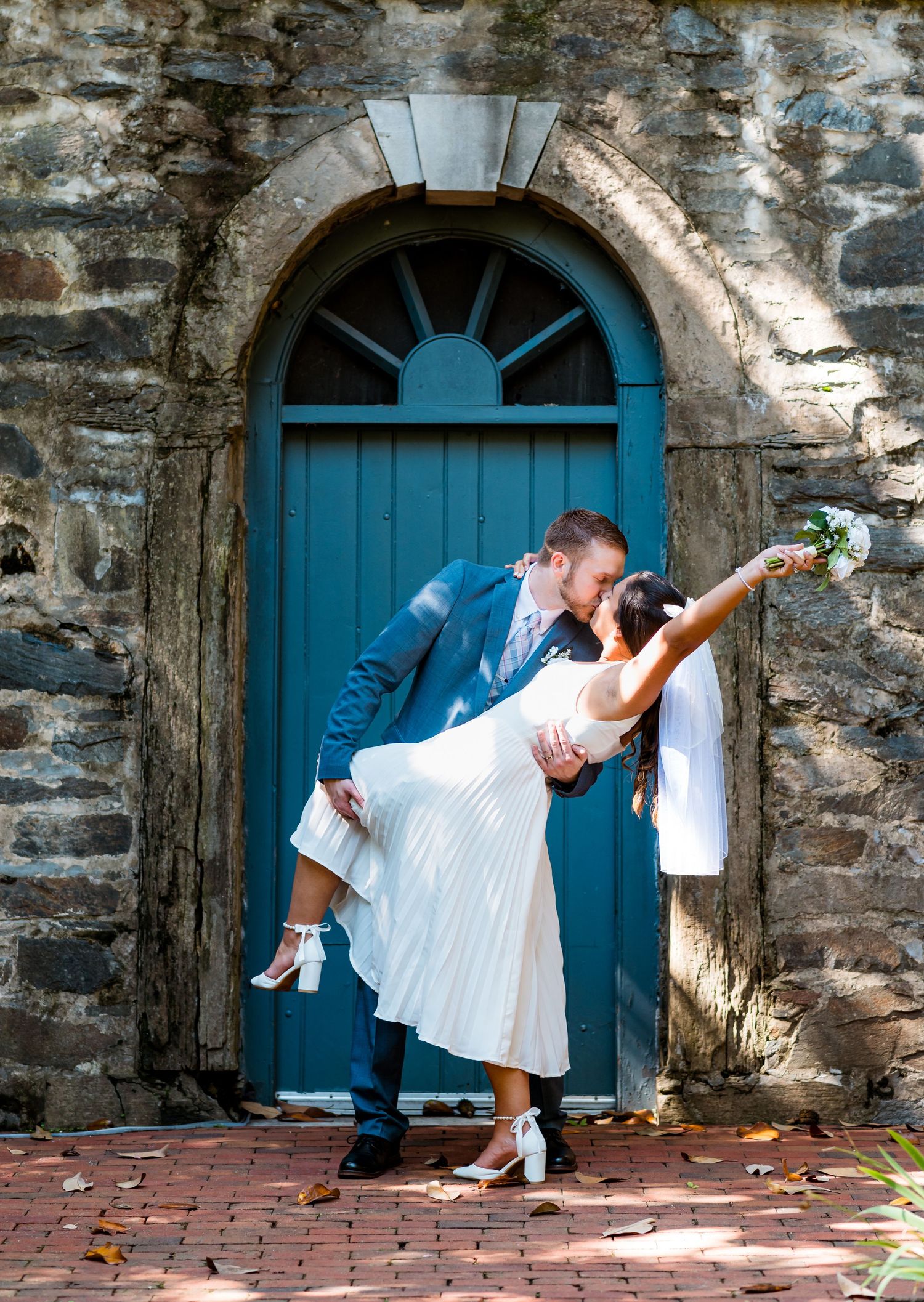 Couple performs romantic dance dip pose in front of vintage blue arched door.
