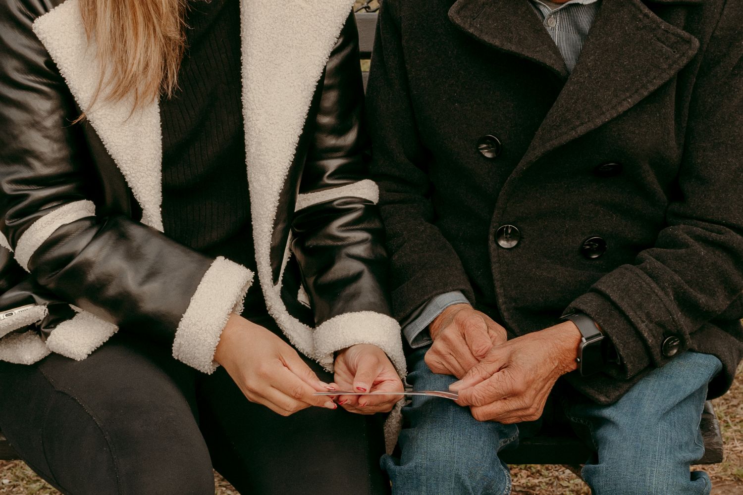 Close-up of hands holding something between two people wearing winter coats.