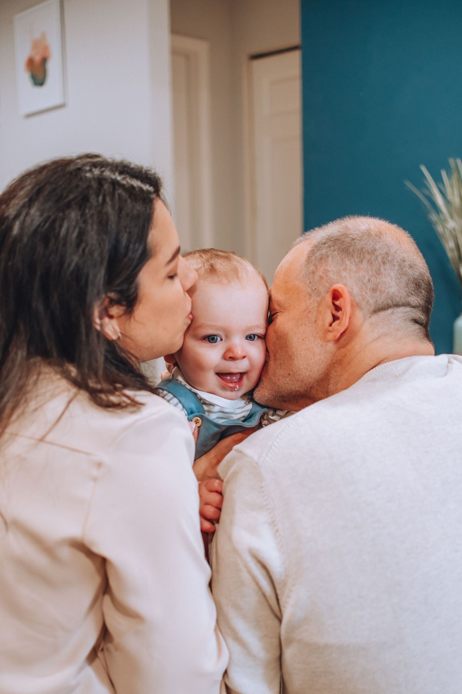 Sweet family moment with baby laughing between kisses in living room.