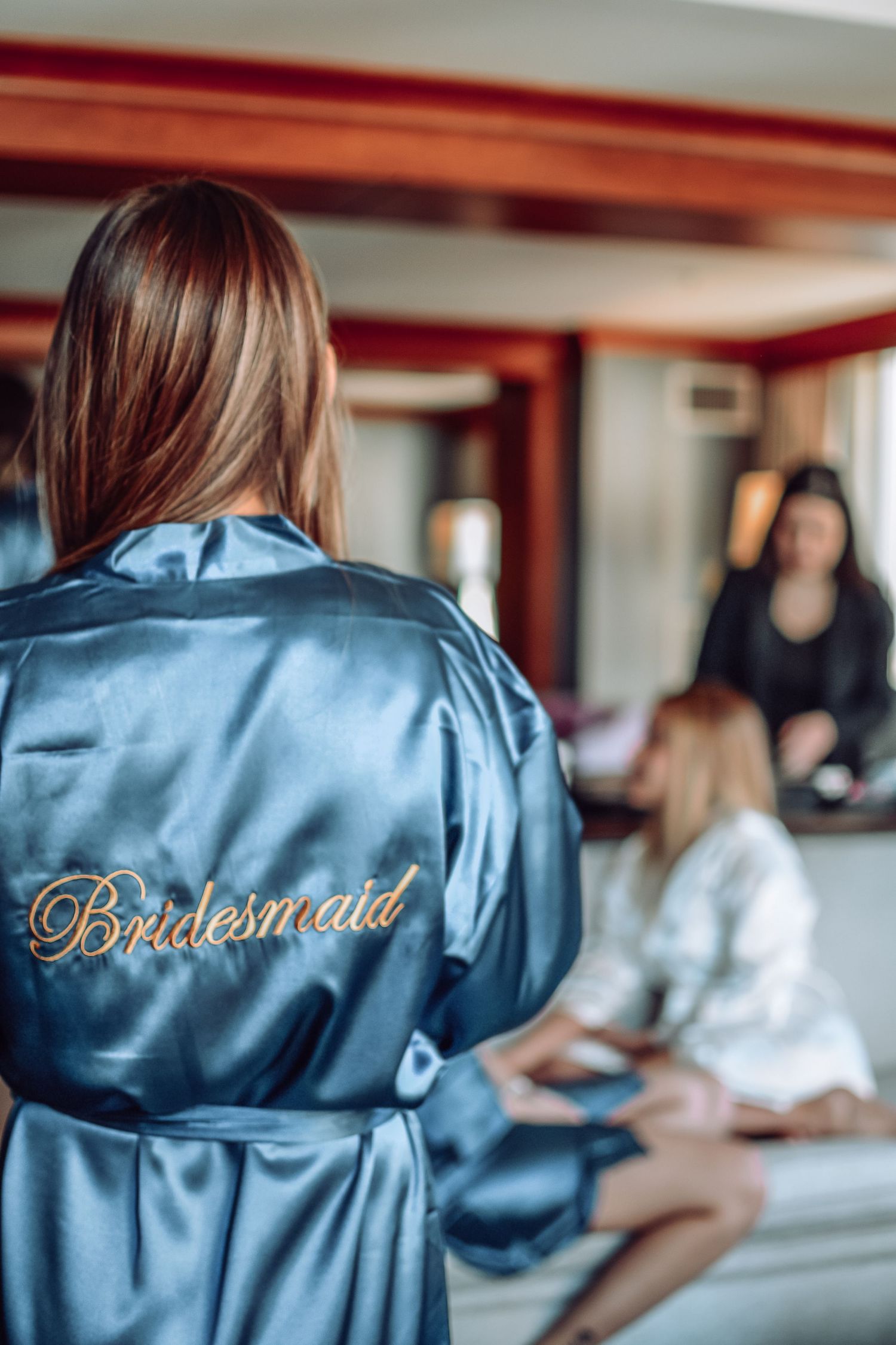 Bridesmaid in light blue silk robe getting ready on wedding morning with others visible in background.