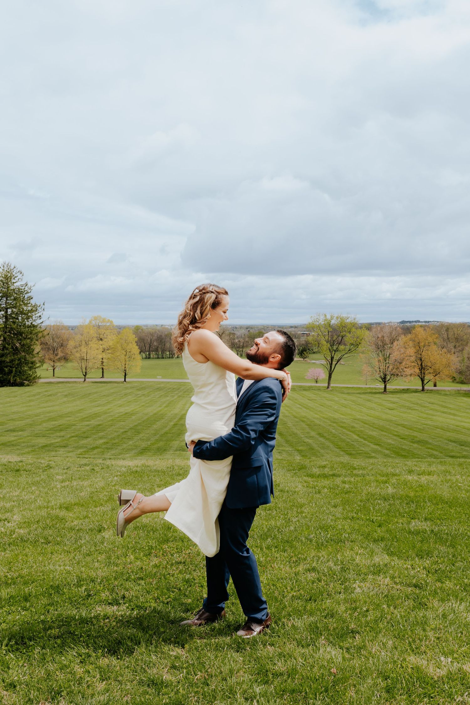 A joyful moment captured as a couple in wedding attire embrace on a lush green hillside.