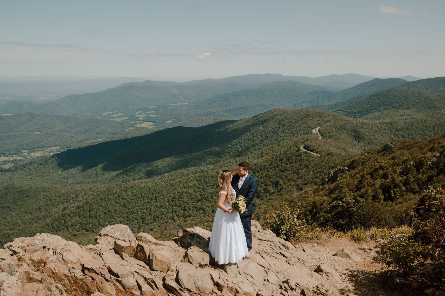 Two people admiring scenic mountain views with a foggy landscape and rolling hills stretching to the horizon.