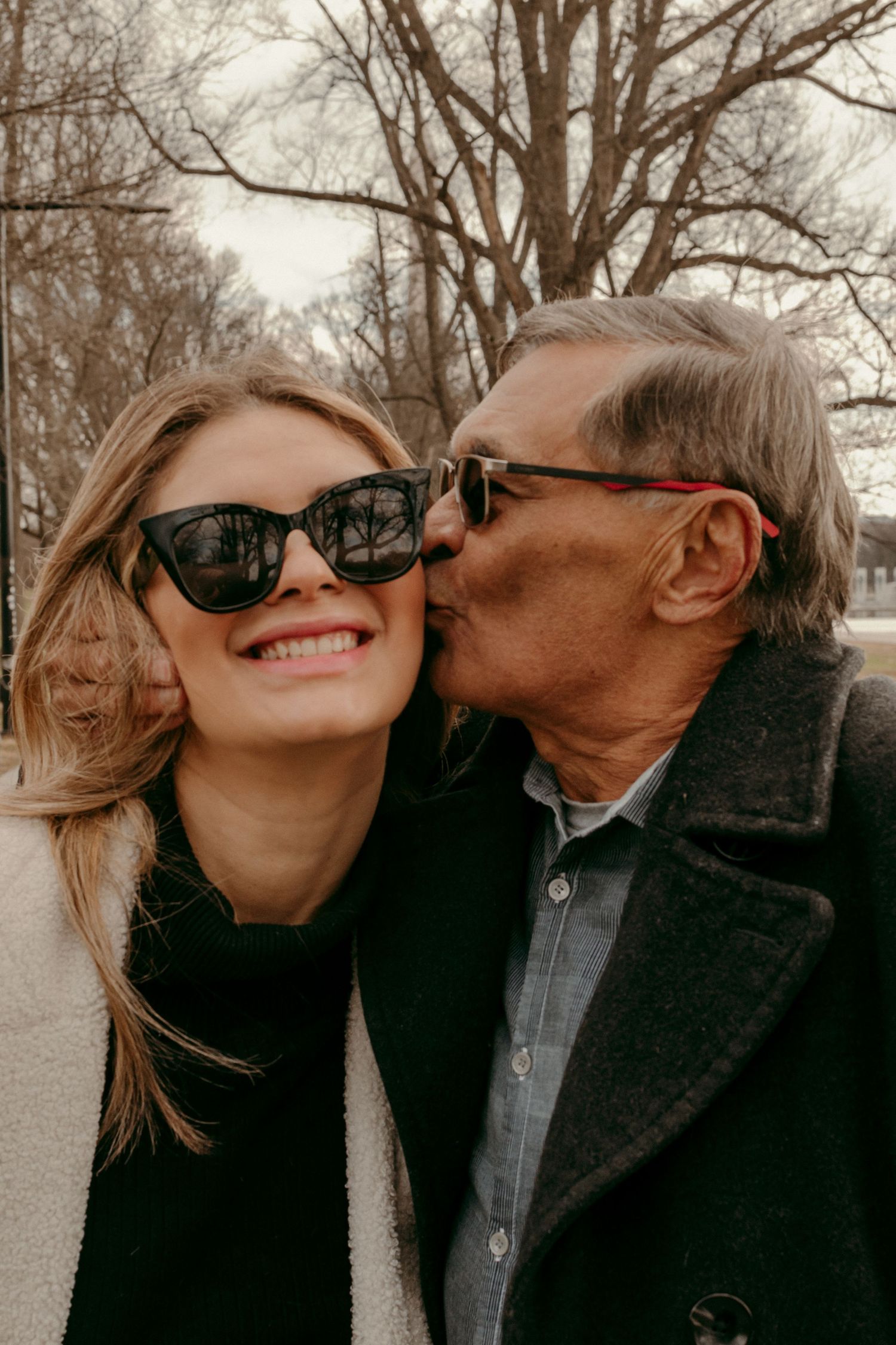 Two people wearing sunglasses share an affectionate moment on a cold day.