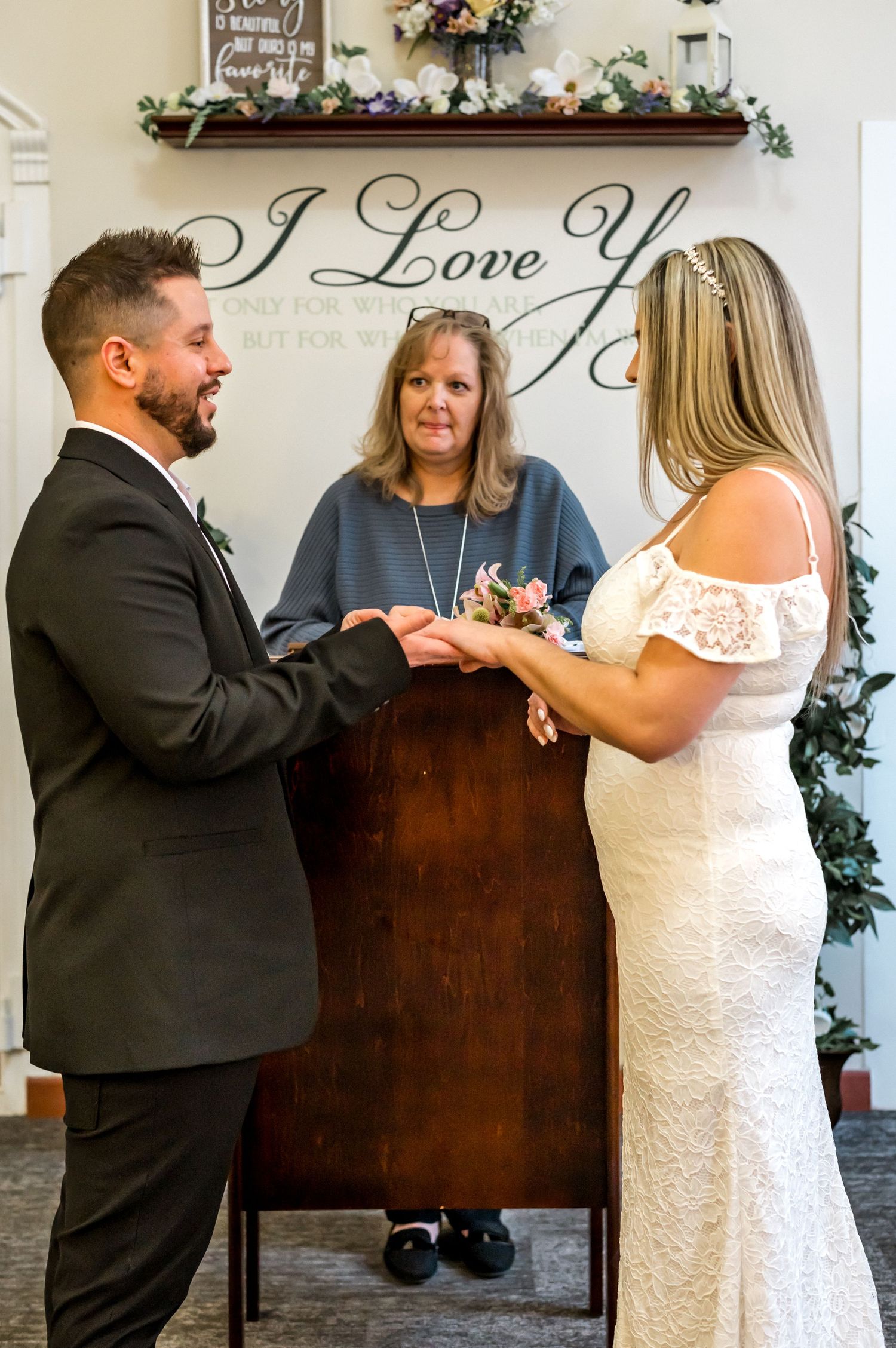 Couple exchanges rings during wedding ceremony under elegant 'I Love You' wall decor.