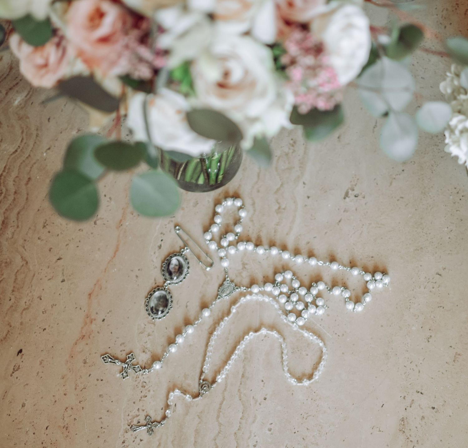 Pearl necklace on a textured beige surface with pink and white flowers in soft focus background.