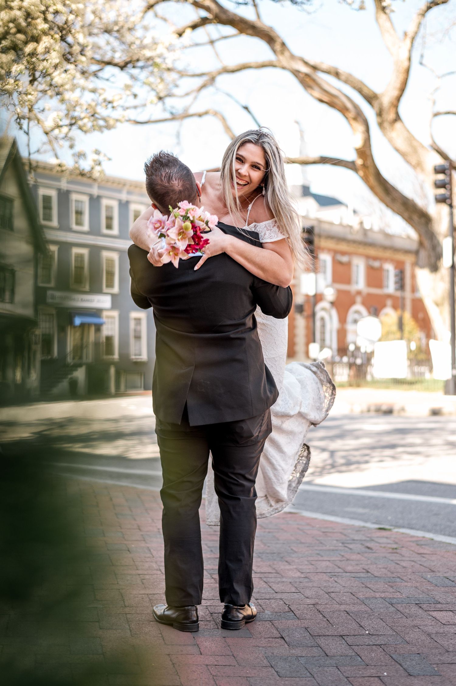 A romantic moment between newlyweds embracing on a brick sidewalk in front of historic buildings.