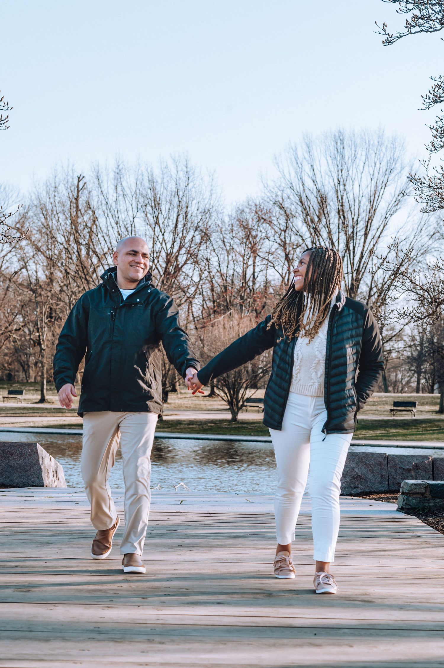 Couple holding hands while walking on wooden boardwalk near lake during winter.
